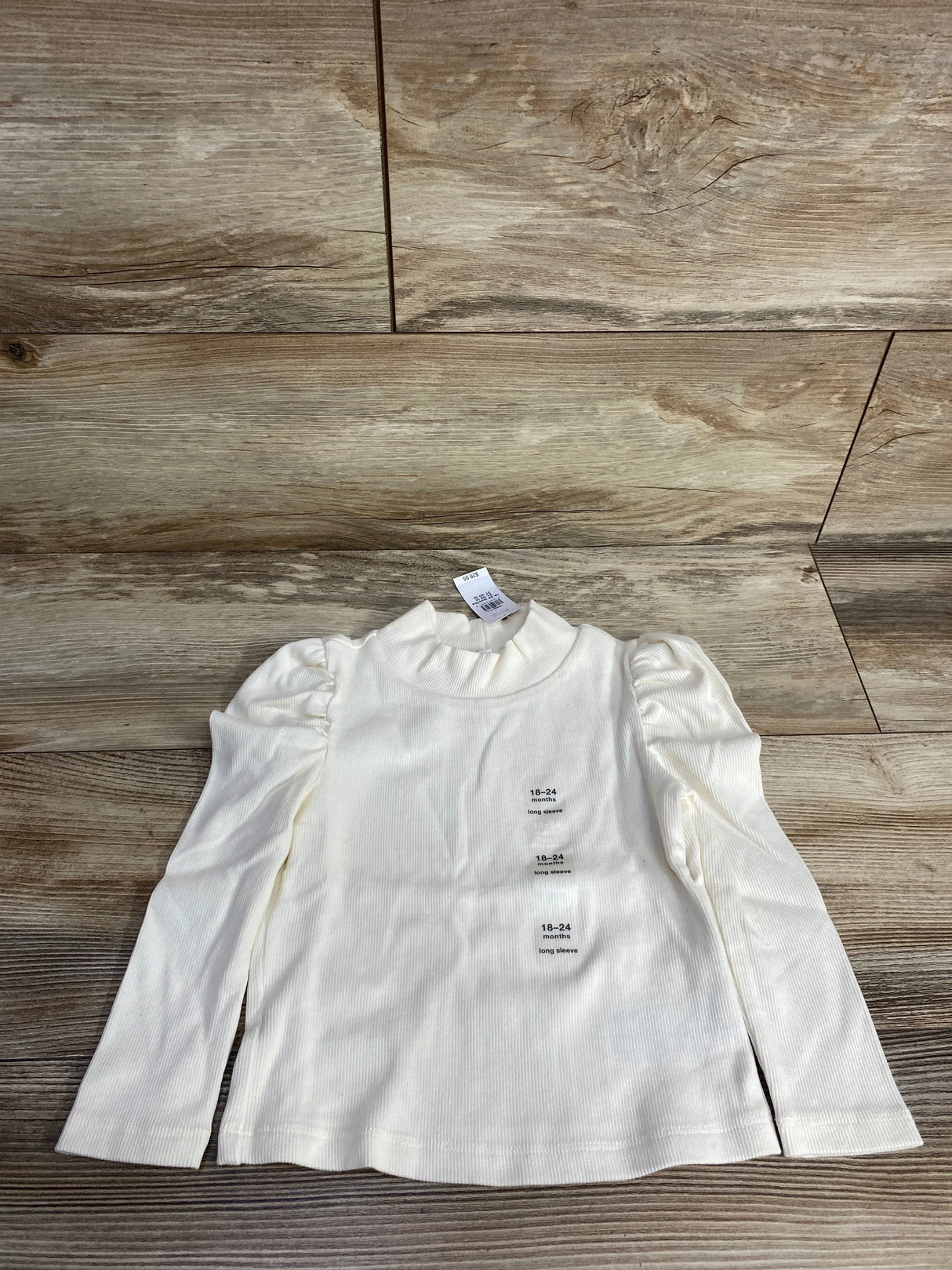 Ivory long sleeve toddler shirt with puff shoulders, size 18-24 months, on wood background