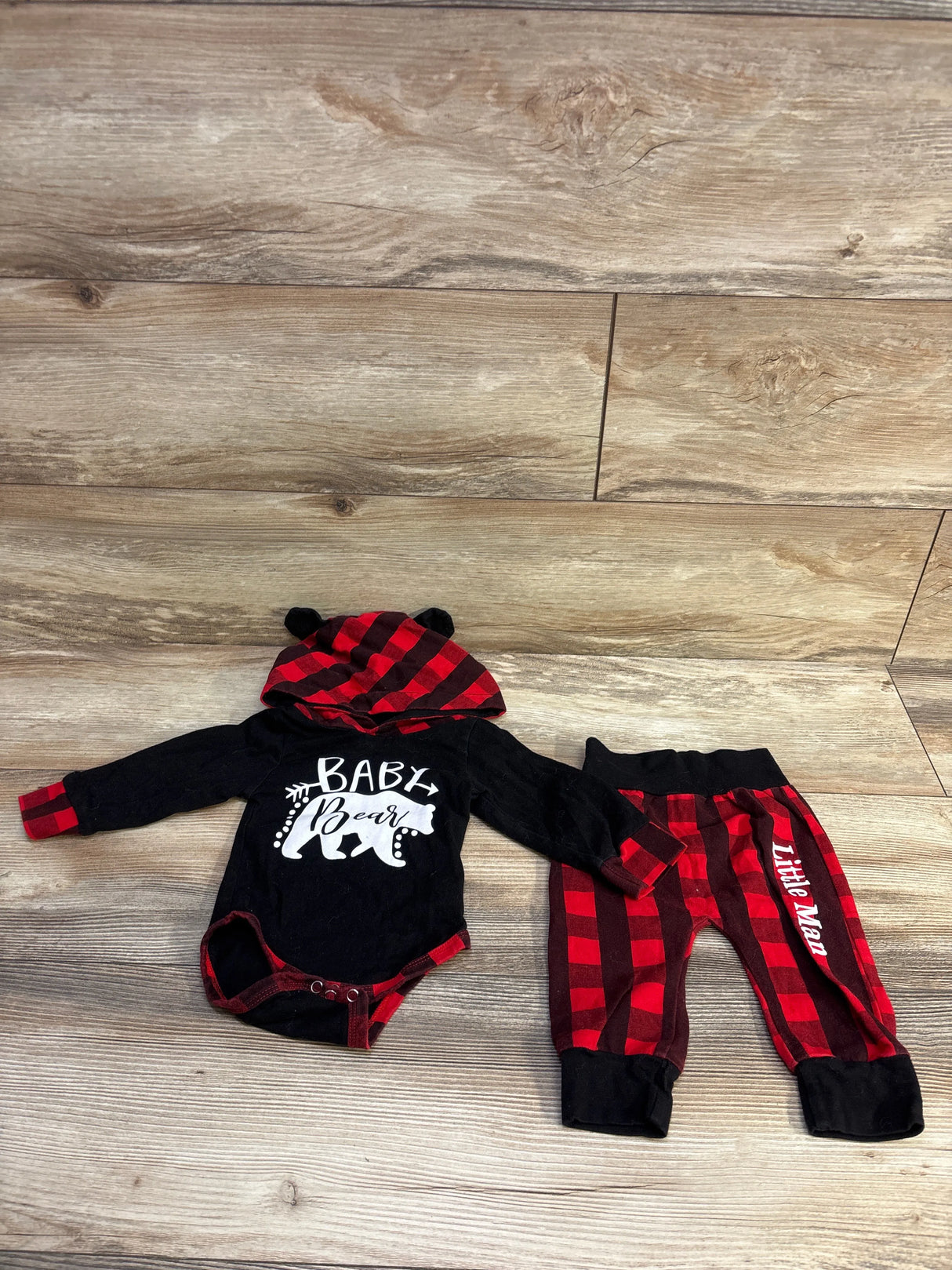 Flat lay of baby set: black hooded bodysuit with white Baby Bear print and red-black plaid hood, matching pants, size 3-6m