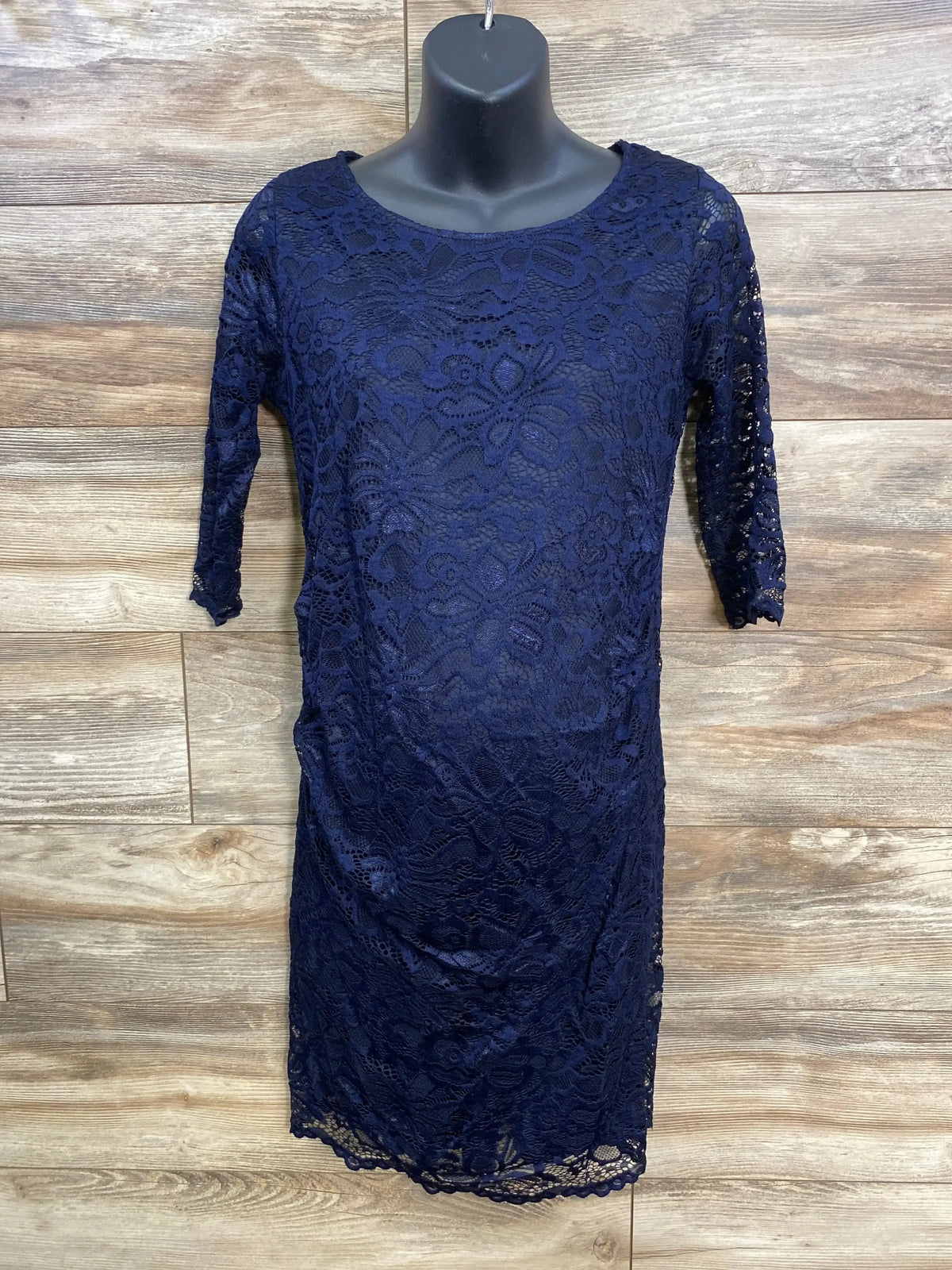 Front view of navy Pink Blush maternity lace dress showcasing floral lace overlay, fitted silhouette, and 3/4 sleeves against wood plank background