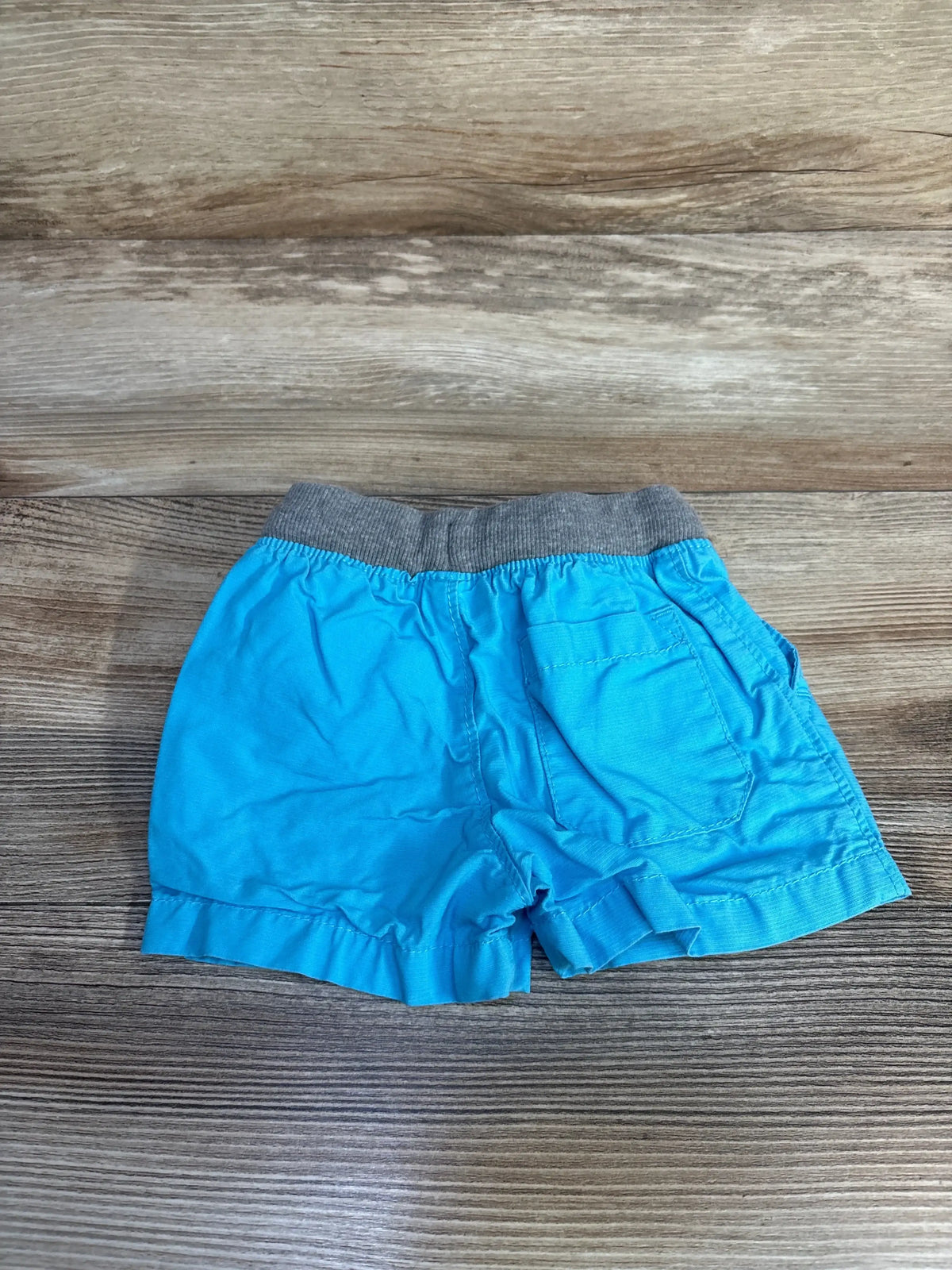 Back flat-lay of blue baby drawstring shorts 3-6 months showing gray elastic waistband and back patch pocket on wood