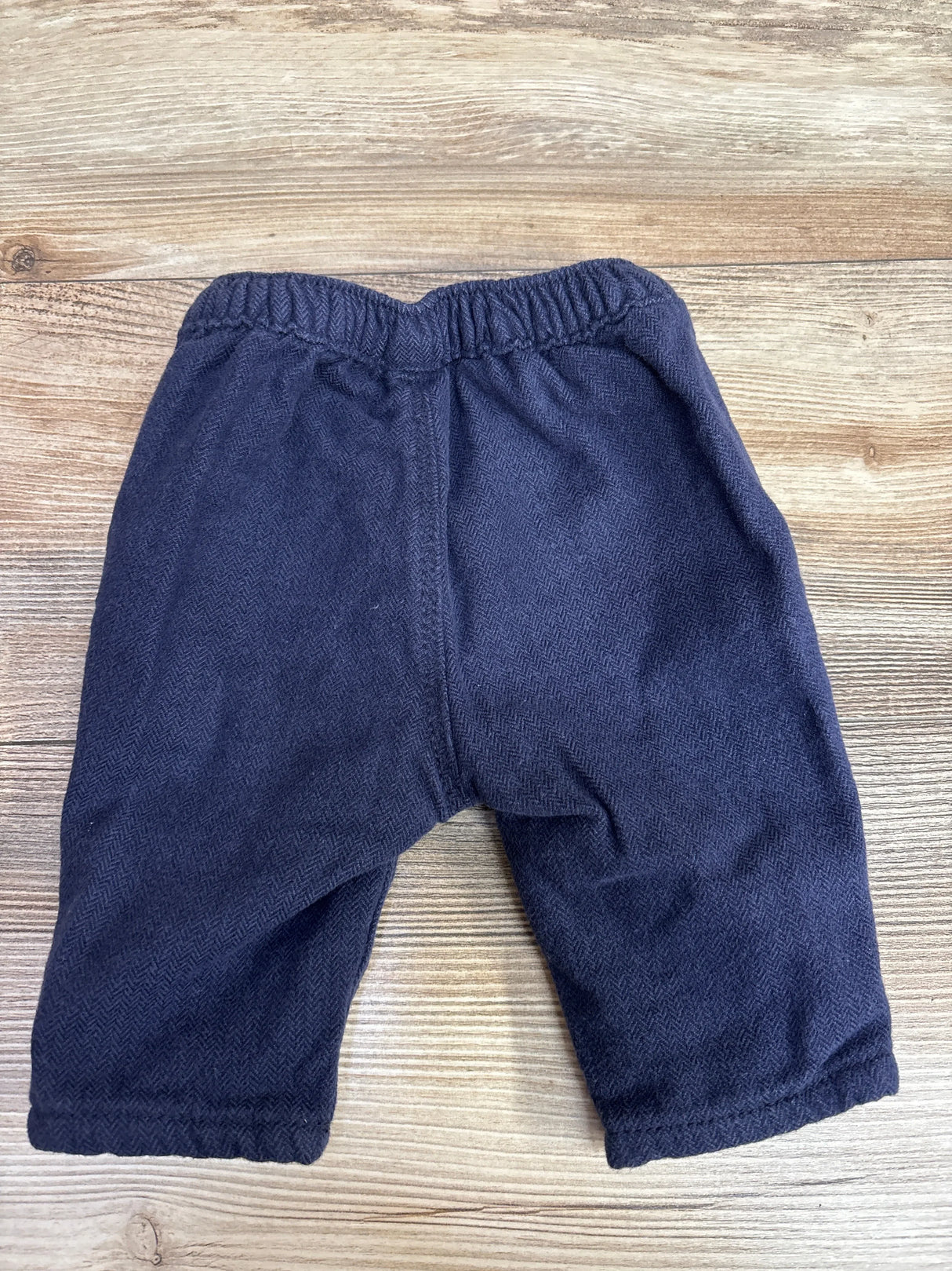 Flat lay of navy OshKosh baby pants showcasing elastic waistband and herringbone tweed texture on light wood background