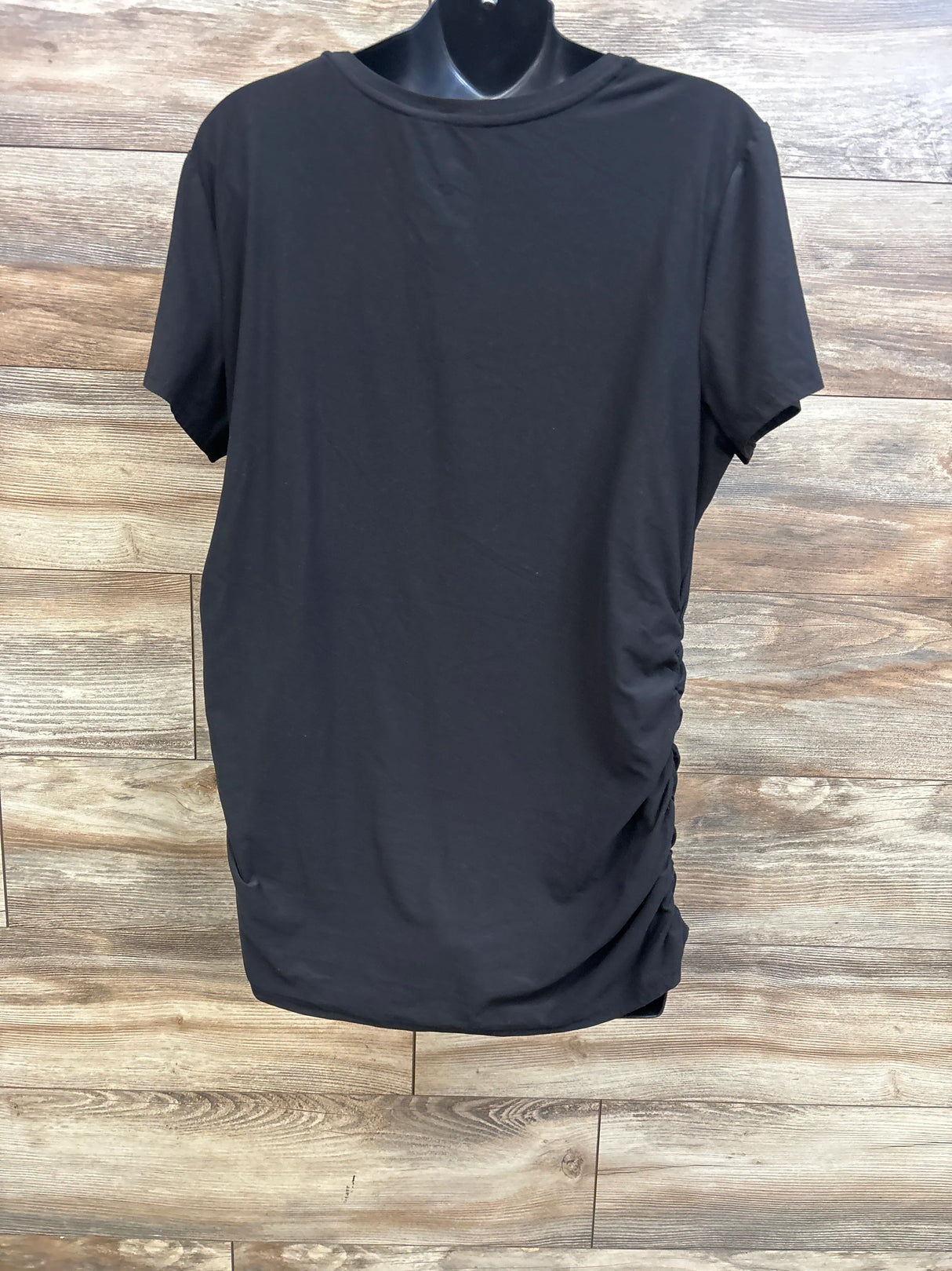 Front view of Time and Tru Mama ruched black maternity shirt showing side ruching and short sleeves on a wood background