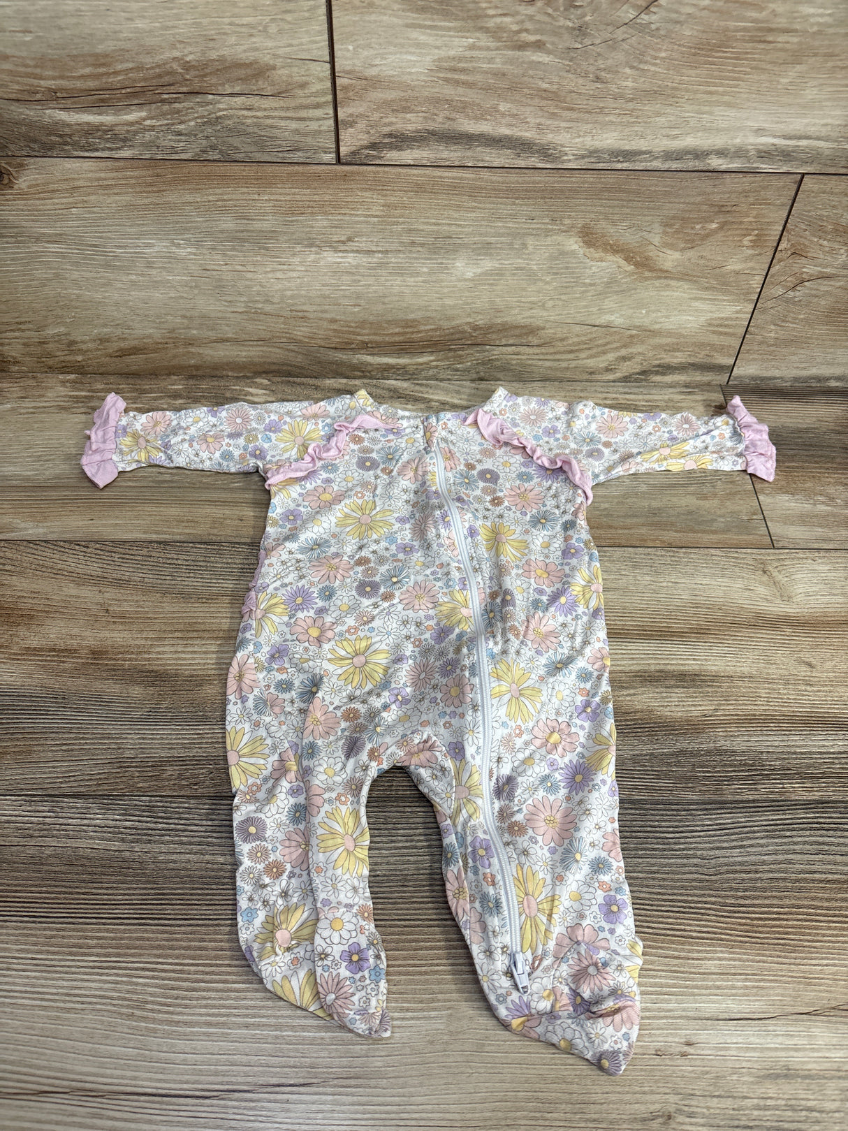 Floral patterned baby sleeper with footies and pink ruffle details laid on wooden floor