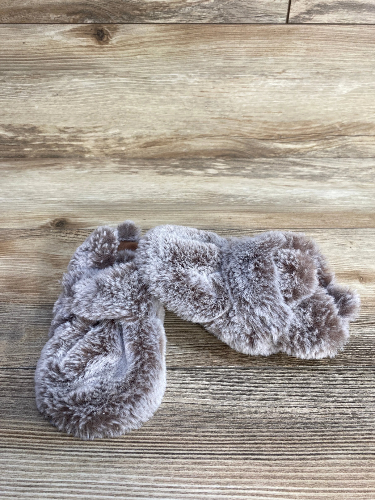 Pair of soft gray faux fur slippers on wooden floor background