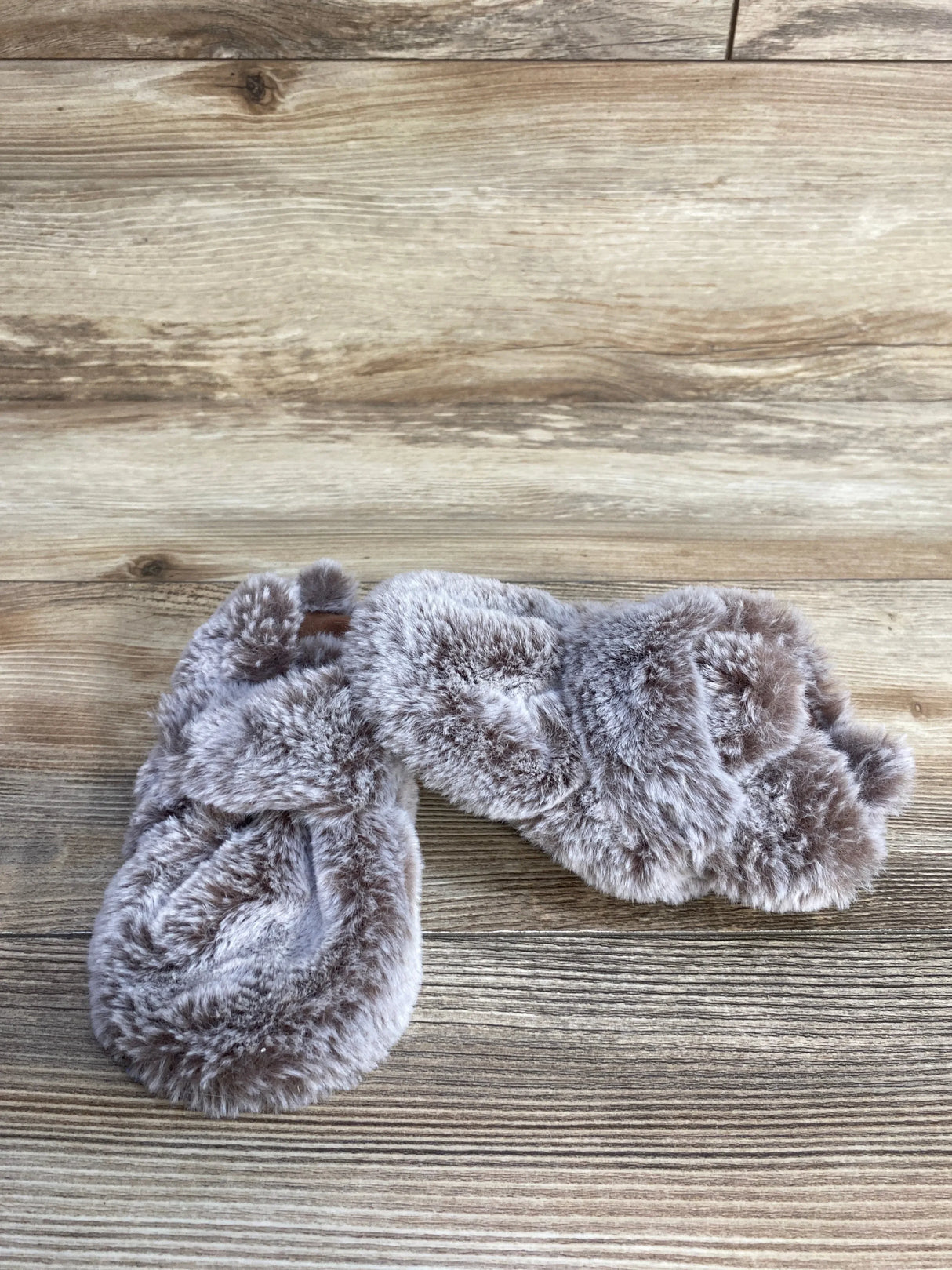 Pair of soft gray faux fur slippers on wooden floor background