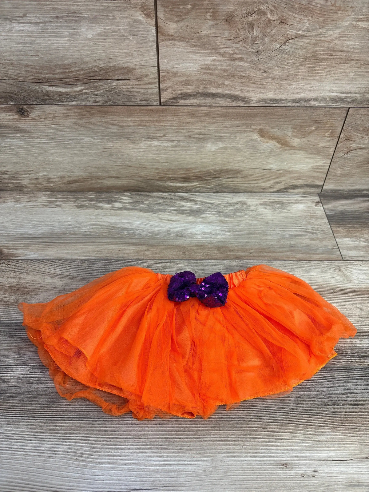 Top view of orange bow tutu in size 0-3m showcasing a purple sequin bow on a wood-look background