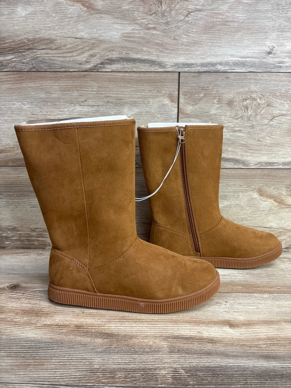 Pair of brown suede children's boots with side zipper and rubber sole on wooden floor