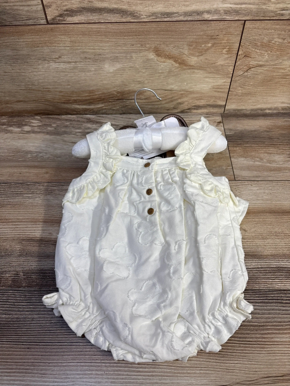 Front view of white Haute Hippie bubble romper showcasing ruffle sleeves and three-button placket on a wood floor