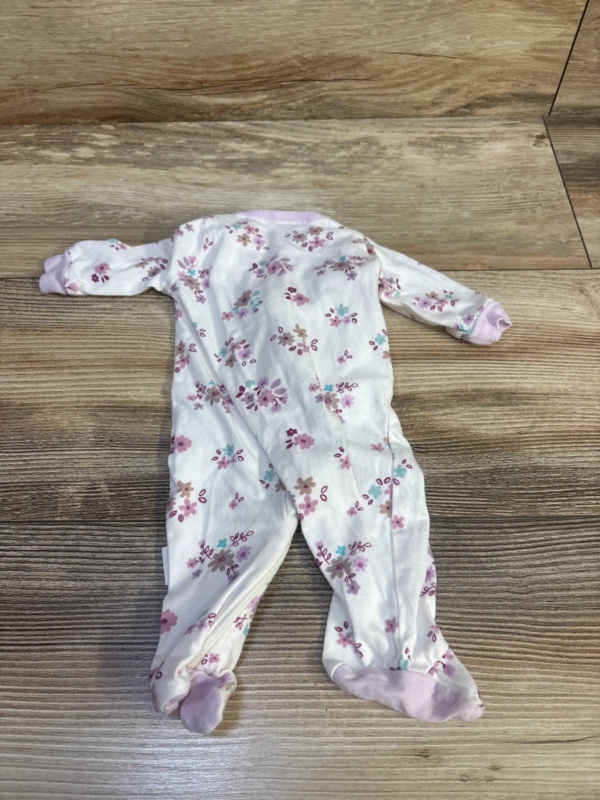 Top view of Gerber preemie sleeper showcasing white floral fabric and lavender cuffs on a wood floor