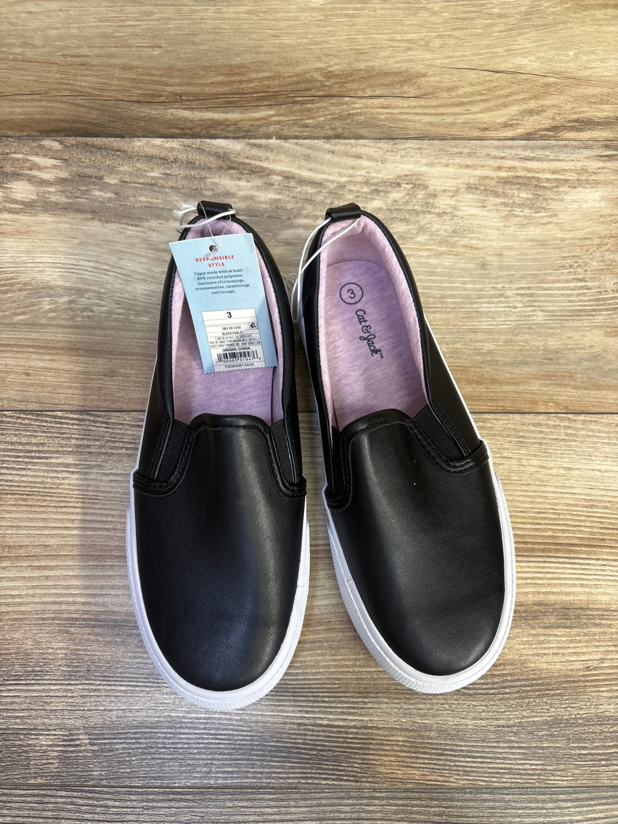 Top-down view of Cat & Jack Hailey toddler slip-on sneakers in black with white sole, pink inner lining and size 3Y tag on wooden floor