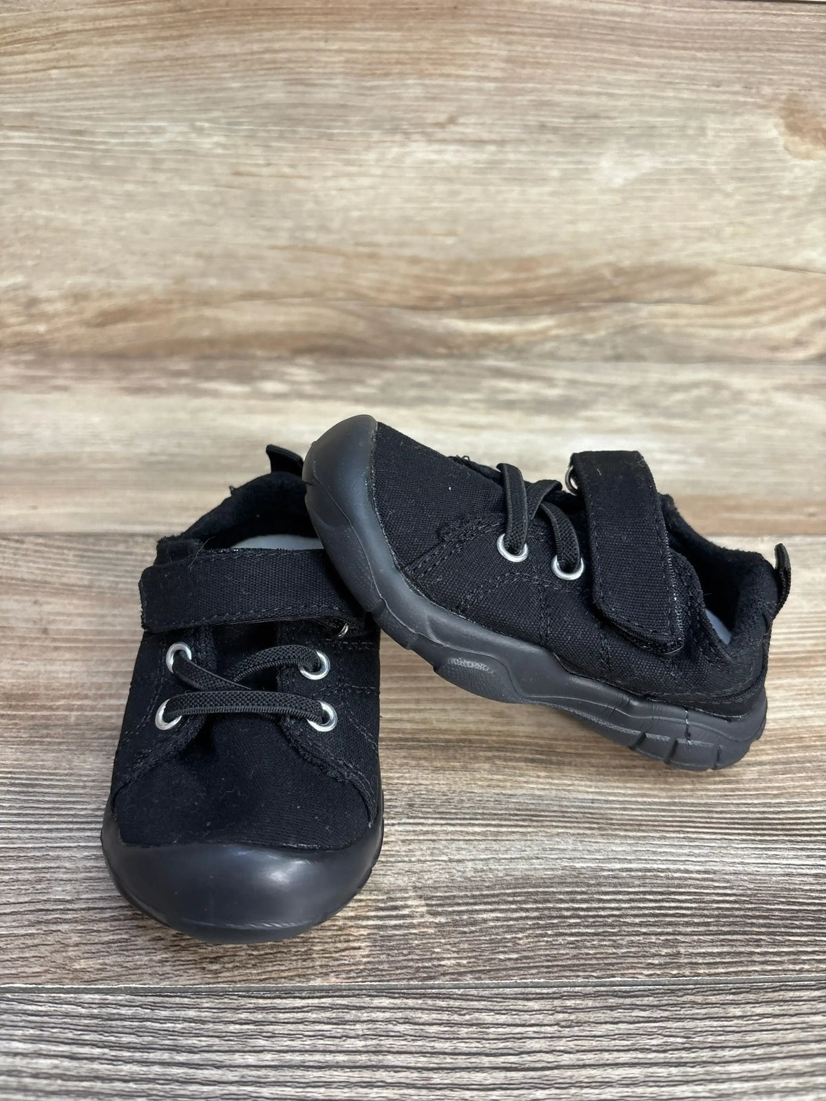 Pair of black toddler shoes with velcro straps and laces on wooden surface