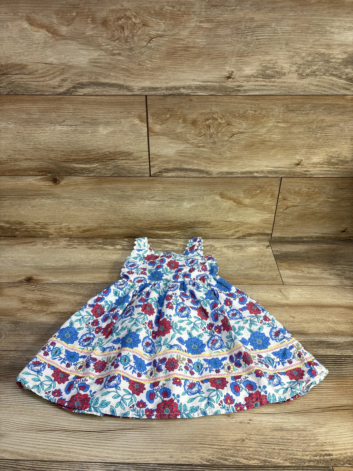 Flat lay Btween girls' white sleeveless dress, blue and red floral print, gathered bodice and full skirt on wood floor