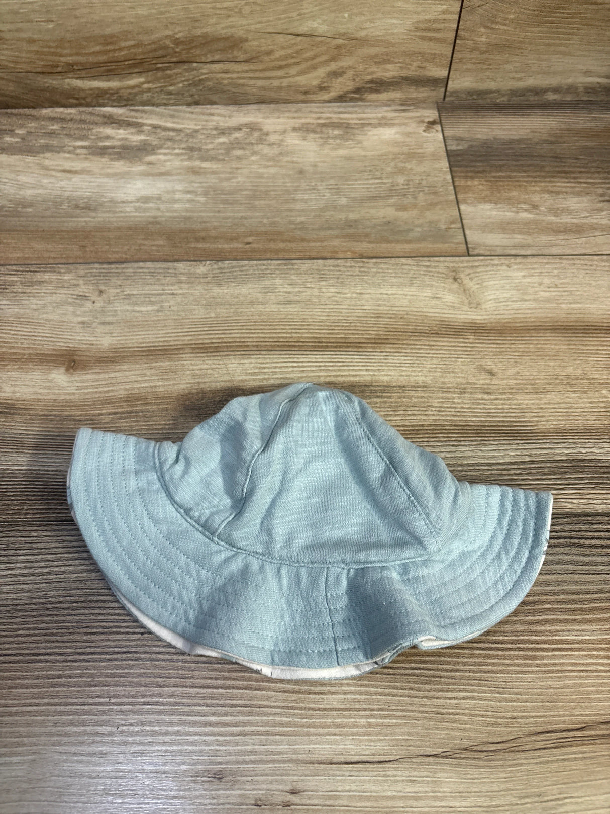 Top-down of Carter’s reversible baby bucket hat, light blue outer with white lining and stitched brim on wood floor, 3-6m