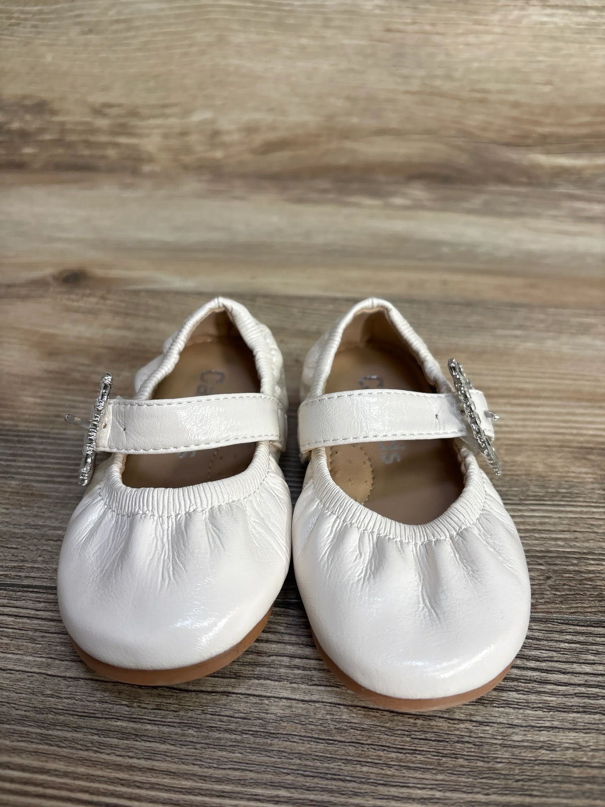 Pair of white baby girl Mary Jane shoes with strap and decorative buckle on wooden surface