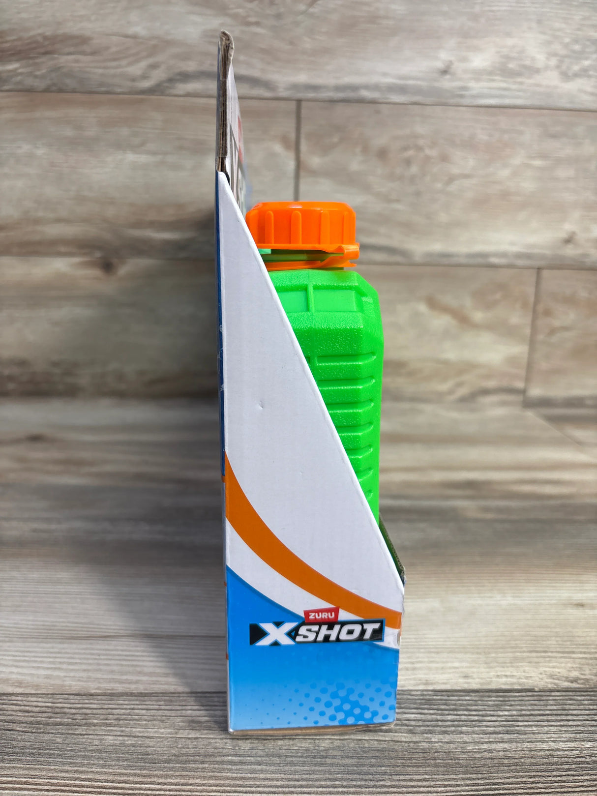 Side view of Zuru X-Shot toy in green and orange packaging on wood floor