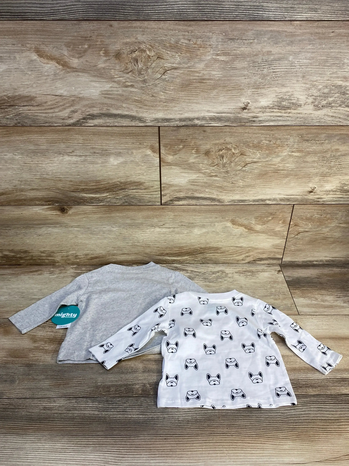 Two long sleeve toddler shirts, one grey and one white with dog print, on wood background