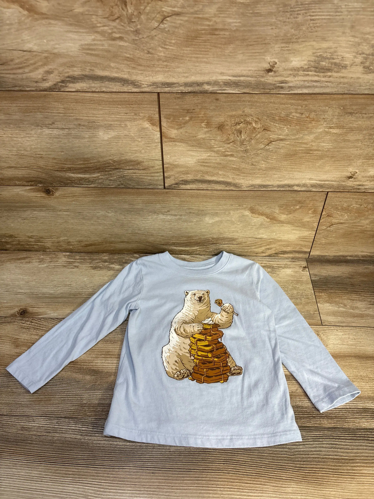Front view of Cat & Jack blue waffle shirt, size 3T, showcasing a bear graphic and long sleeves on a wood surface