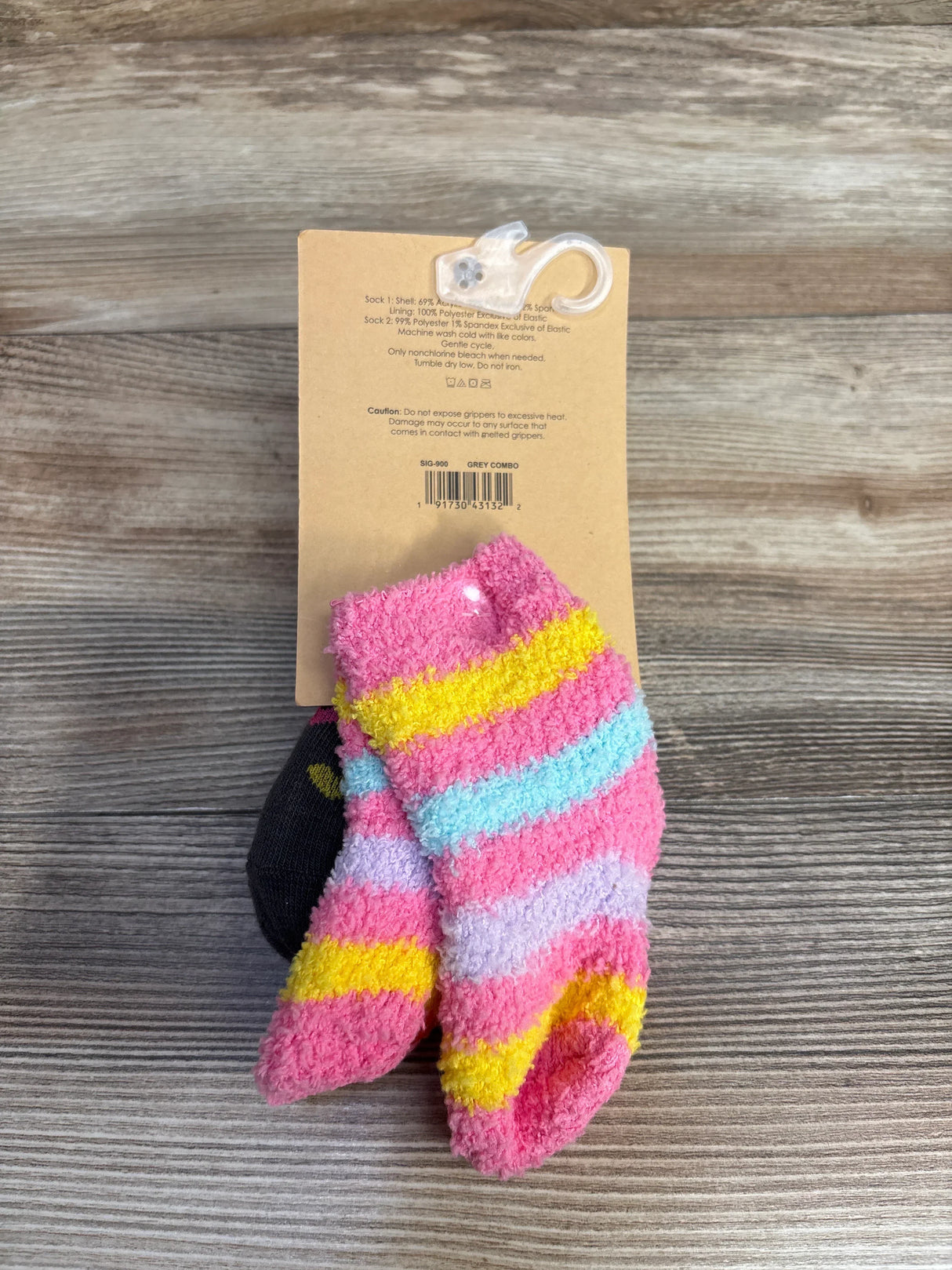 Front view of Capelli slipper socks 2-pack showcasing pink fuzzy striped sock and black gripper sock on wood plank floor