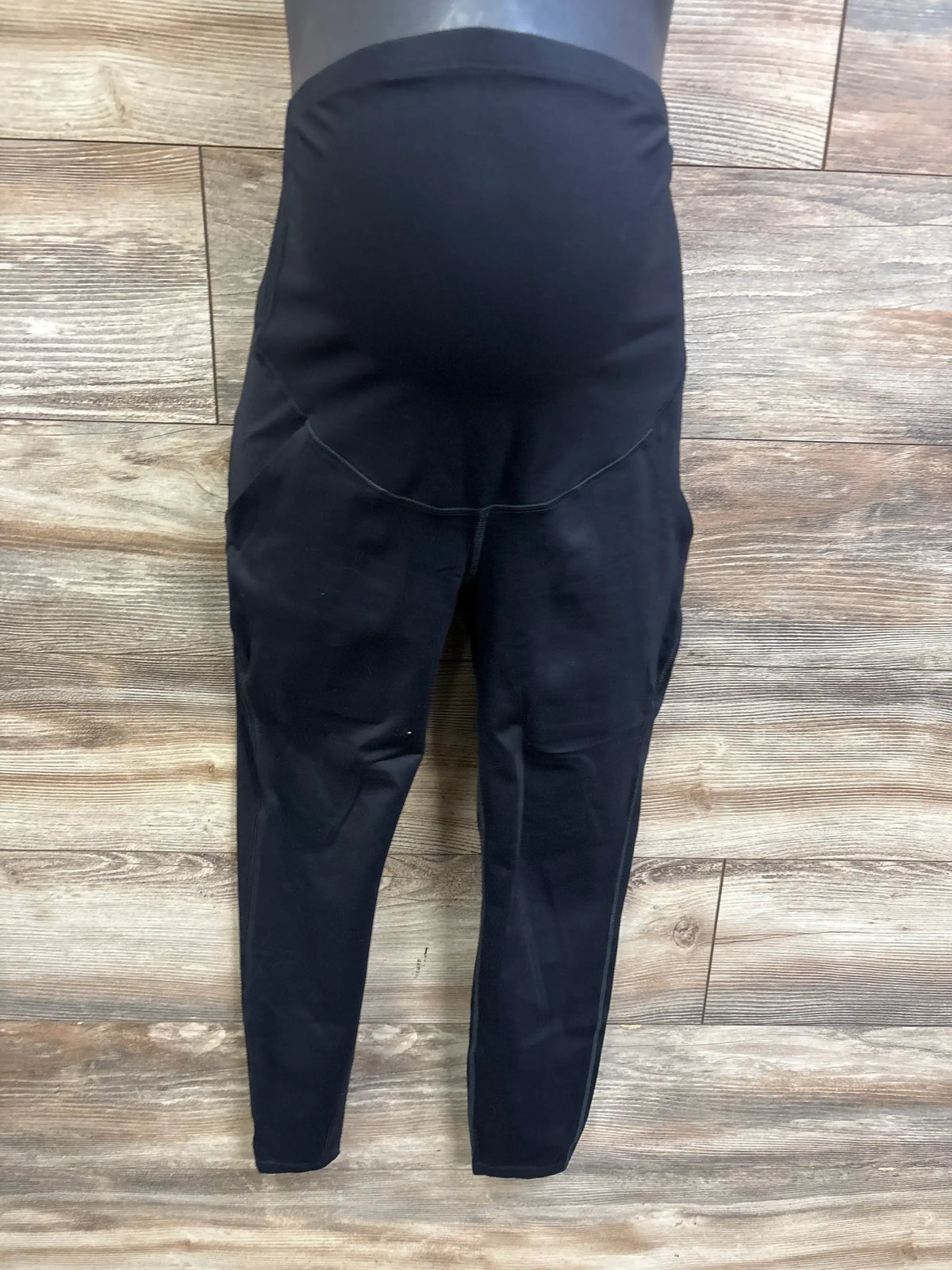 Front view of black maternity leggings showcasing high-rise over-belly panel and tapered legs against a wood floor background