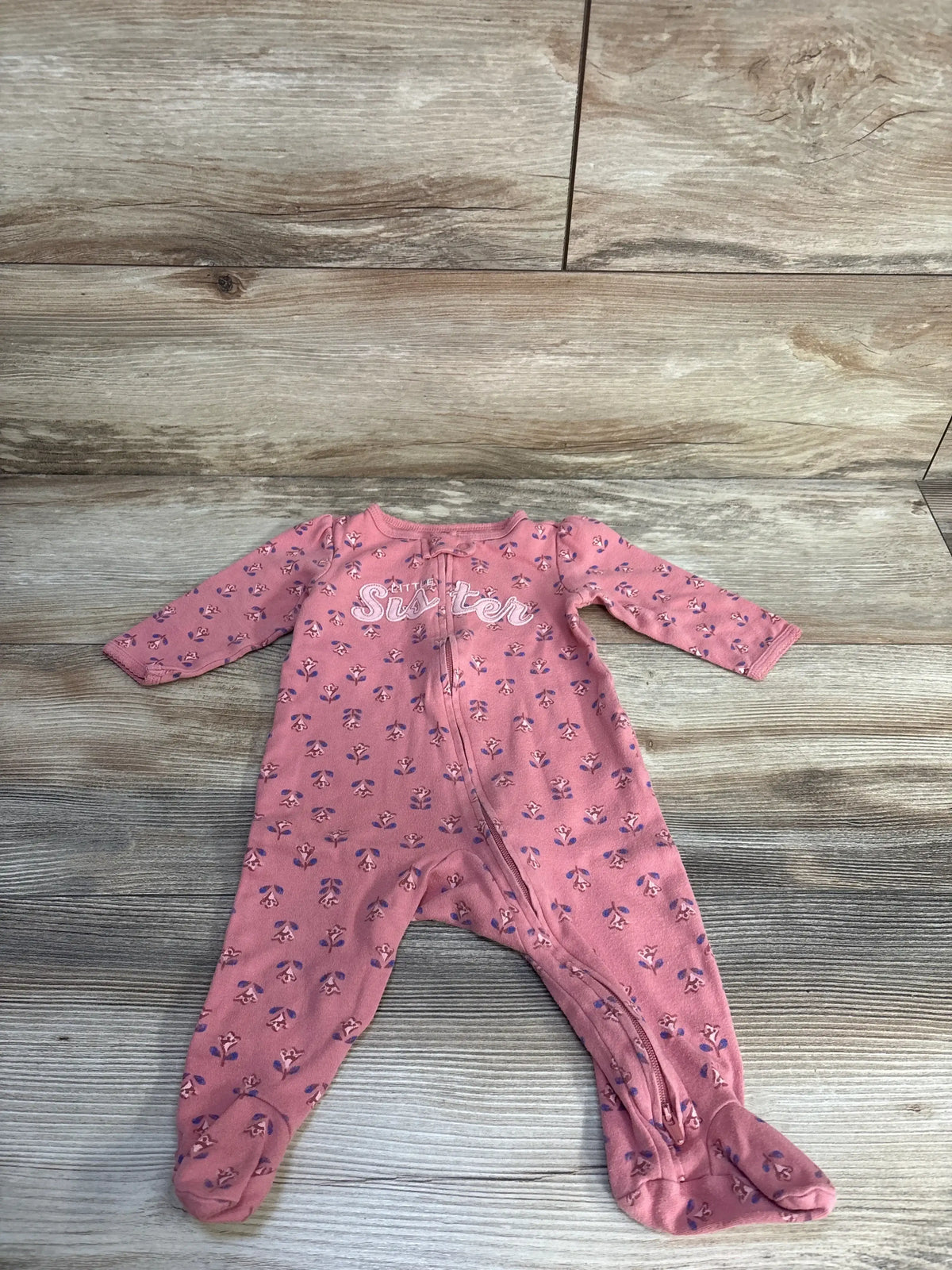 Flat lay of Carter's pink footed sleeper with purple floral print, Little Sister chest embroidery and zipper on wood