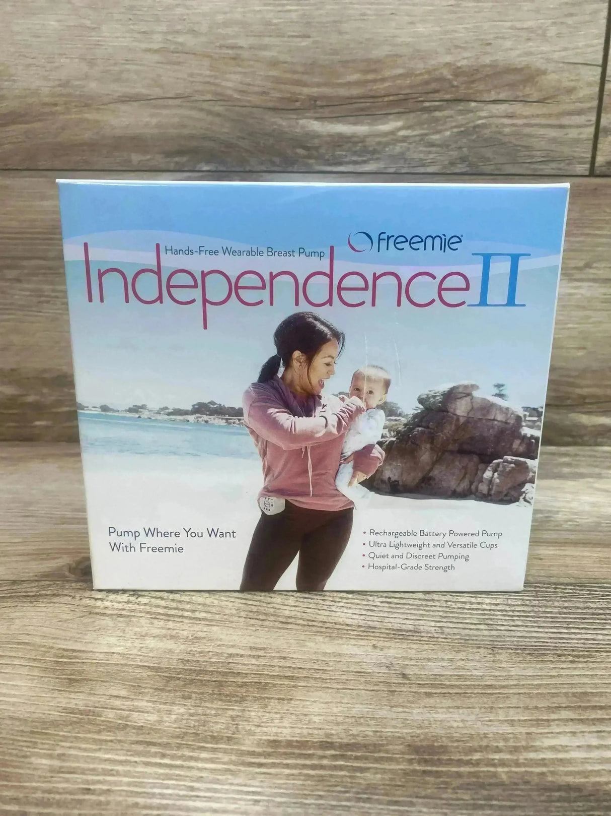 Front view of Freemie Independence II breast pump box showing large “Independence II” title and a photo of a mother holding a baby on a wooden tabletop background