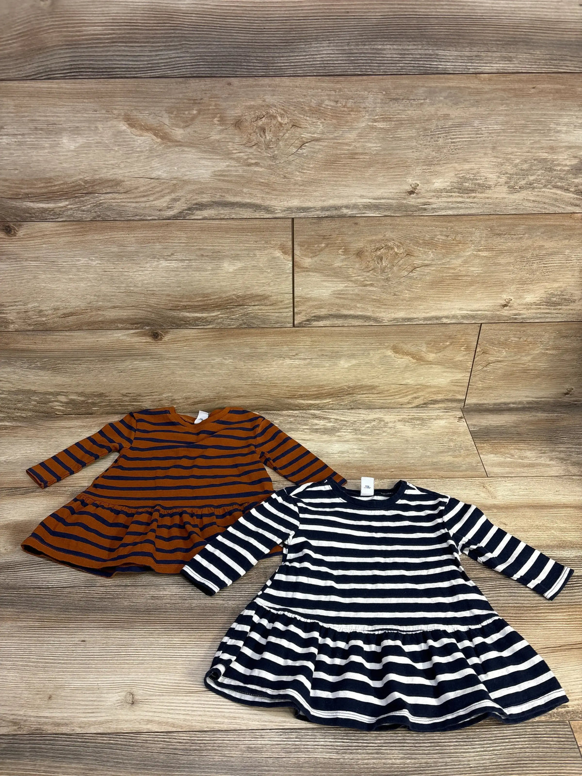 Flat lay of two Old Navy striped peplum tunics with long sleeves and peplum hem, navy/white and rust/navy on wood floor