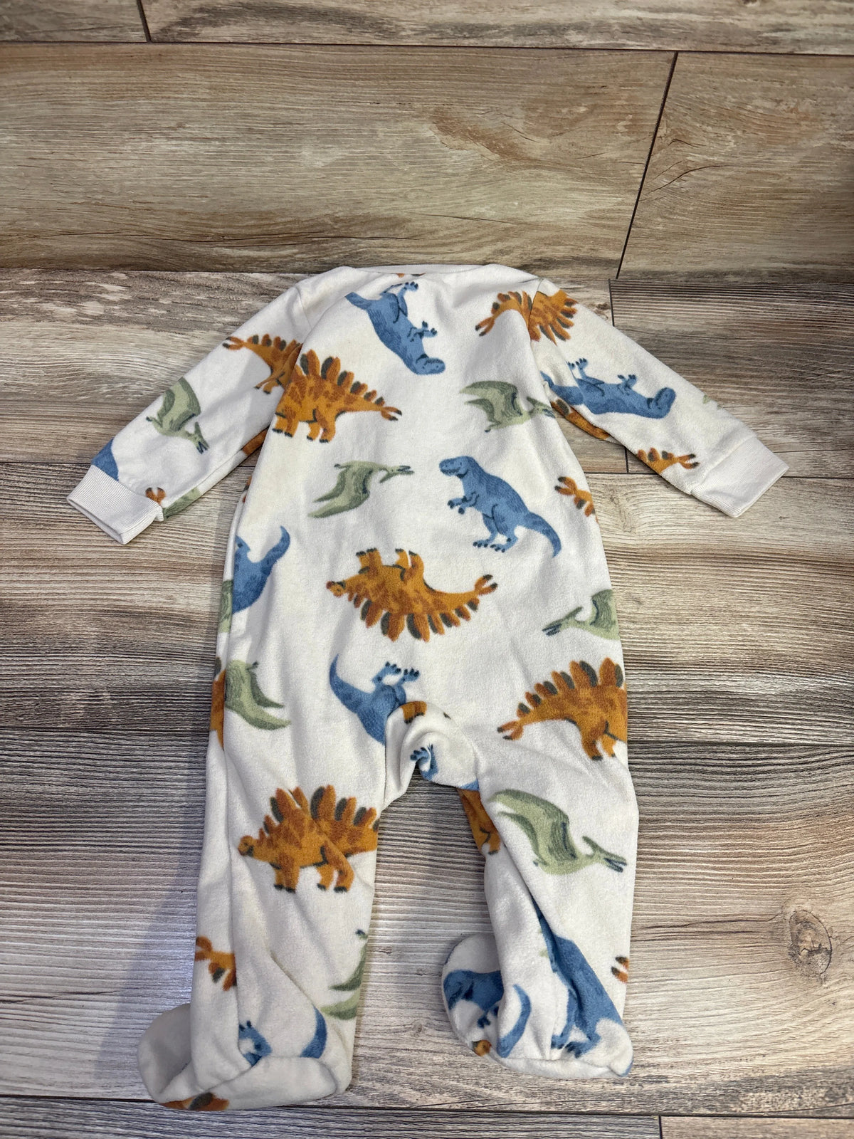 Front view of Carters beige blanket sleeper in size 6 months with long sleeves, footed legs, and dinosaur print on a wood floor