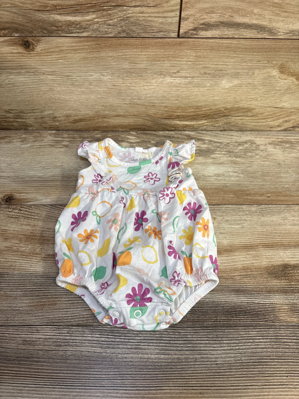 Front view of Okie Dokie white floral bubble romper showcasing colorful floral print and bubble hem on a wood-grain background