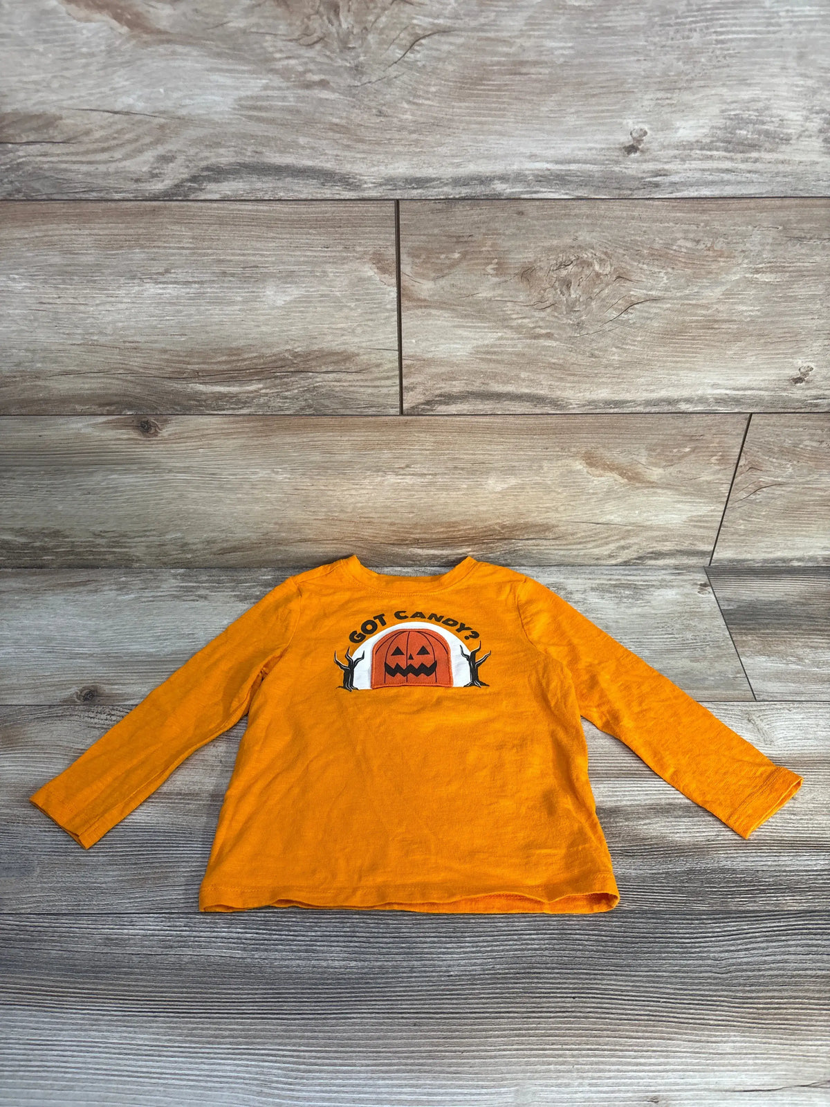 Front view of Old Navy orange toddler Halloween shirt showcasing the Got Candy? pumpkin graphic and long sleeves on a gray wood background