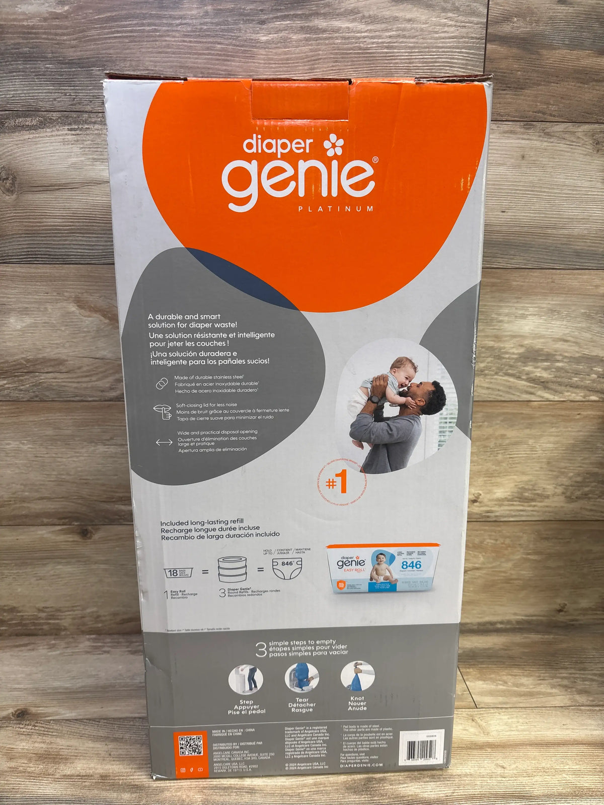 Back of Diaper Genie Platinum Pail box showing refill contents and three-step emptying instructions on a wood floor