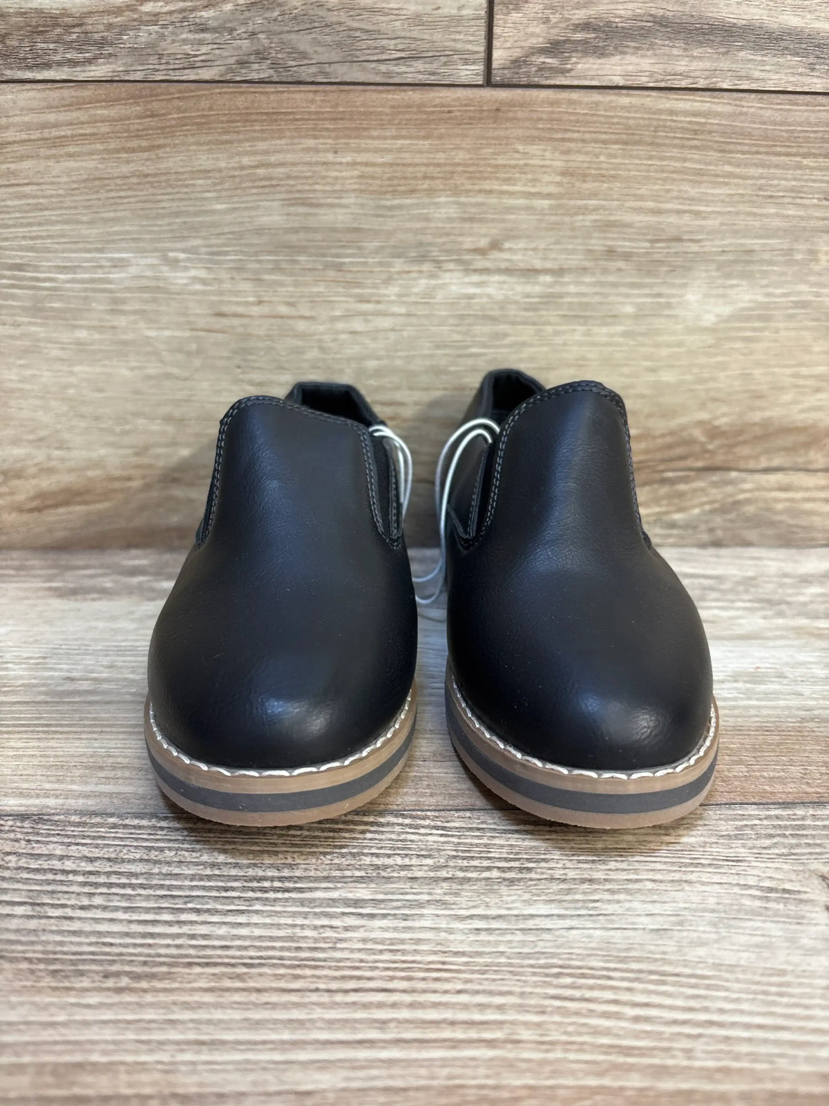 Front view of Cat and Jack Neal black toddler slip-on loafers showing tan layered soles and white topstitching on wooden background