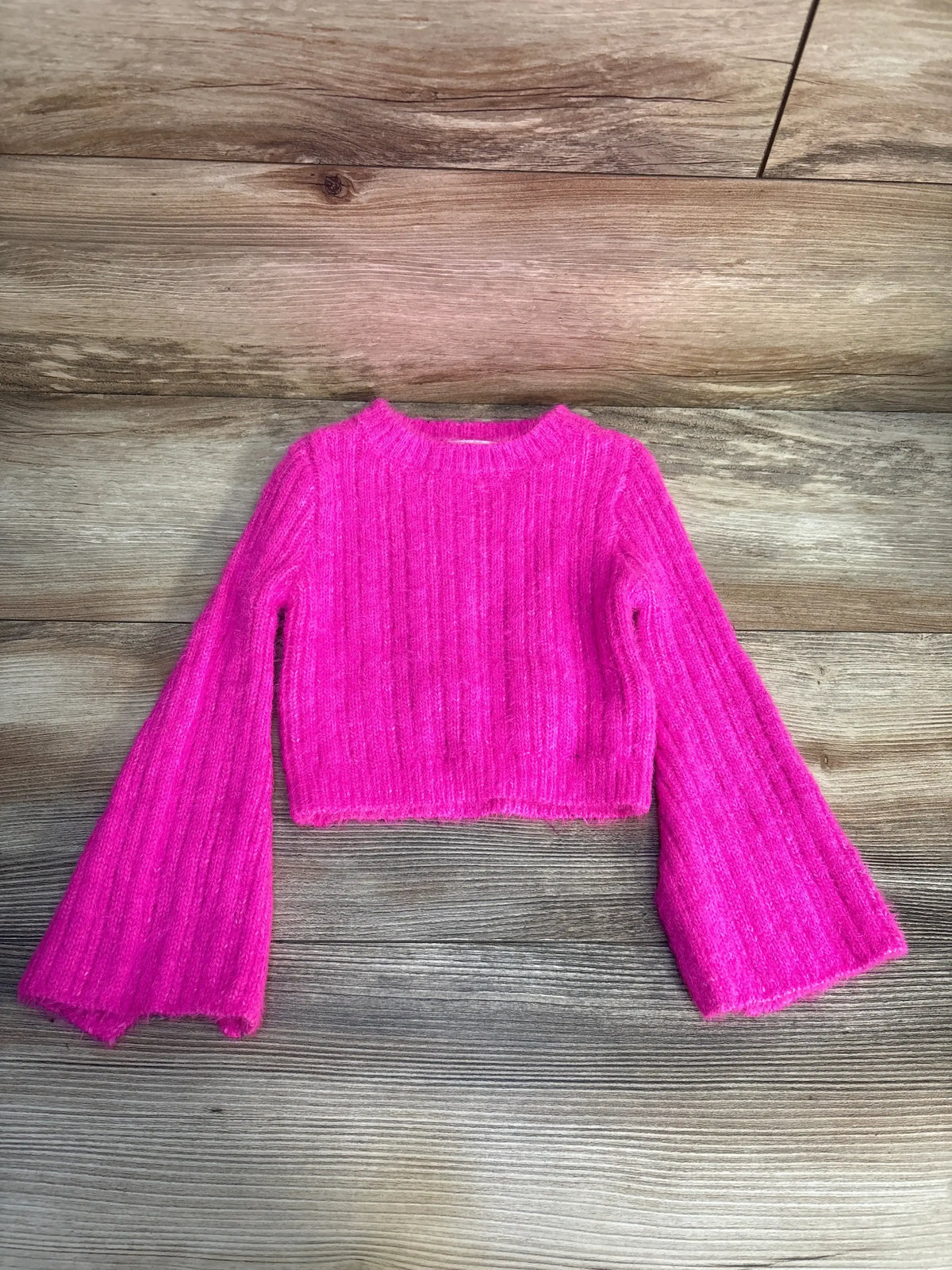 Bright pink ribbed knit long sleeve crop sweater for kids on wooden background