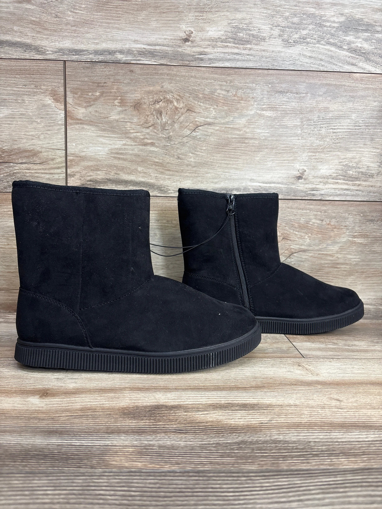 Black suede kids ankle boots with zipper detail on wooden floor background