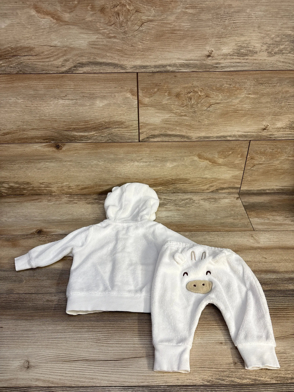 Top view of Carter’s white terry cloth hoodie and matching joggers set on a wood floor, showing hood and animal face detail