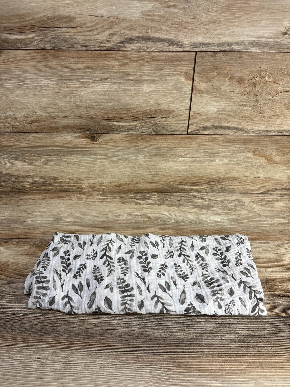 Folded white muslin cloth with gray leaf pattern on wooden surface