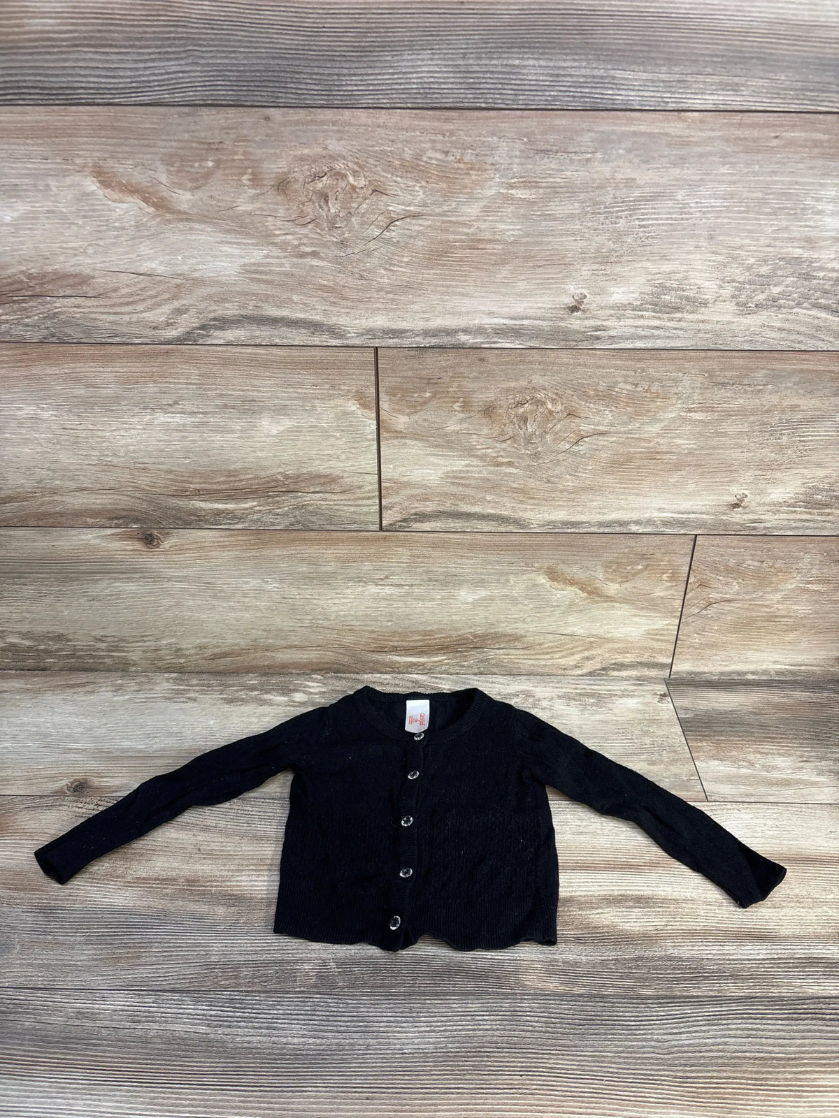 Front view of Cat & Jack black knit cardigan, size 12 months, with long sleeves and button front on wood-look flooring
