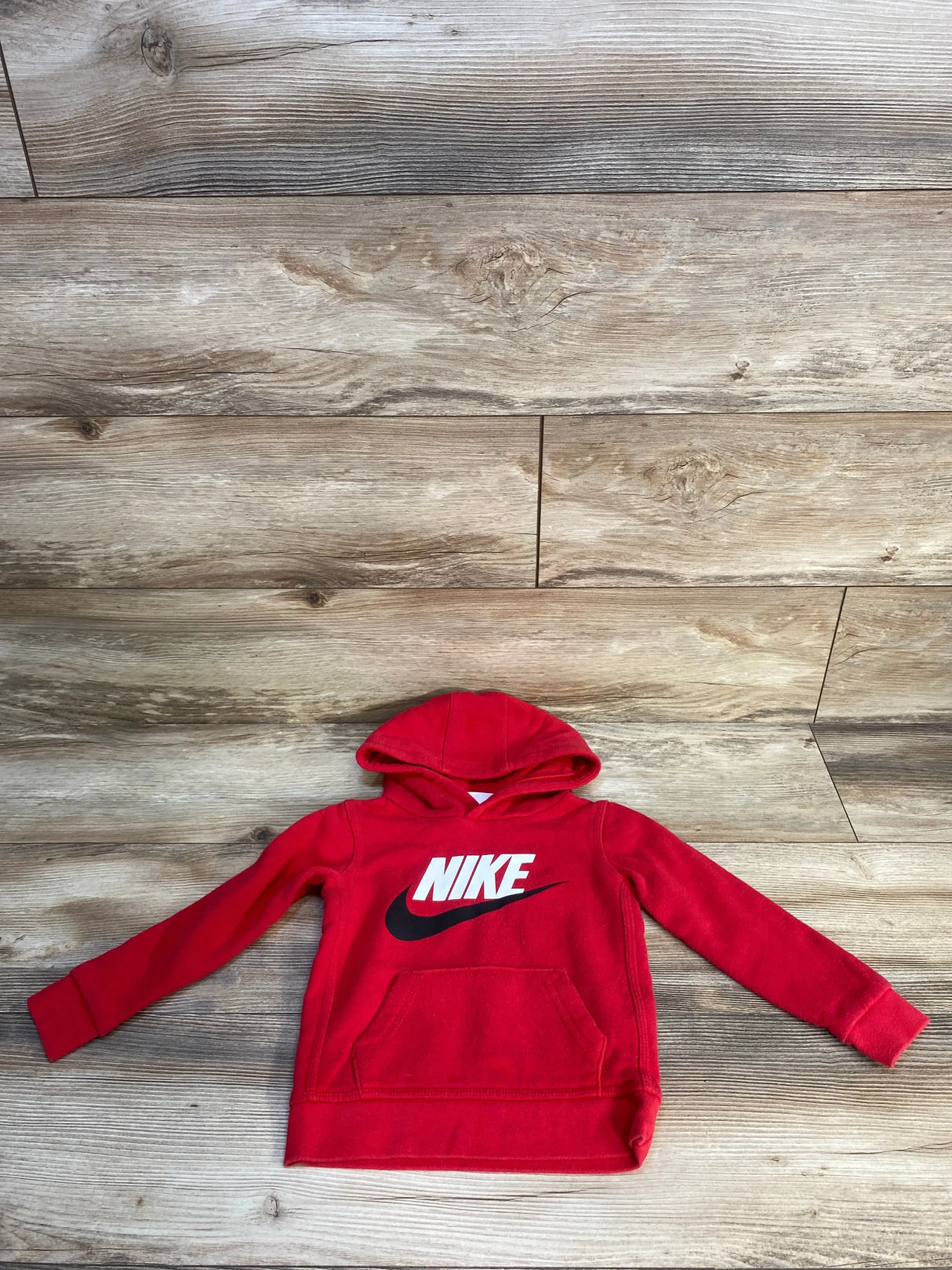 Red Nike kids hoodie with white logo and front pocket on wooden floor background