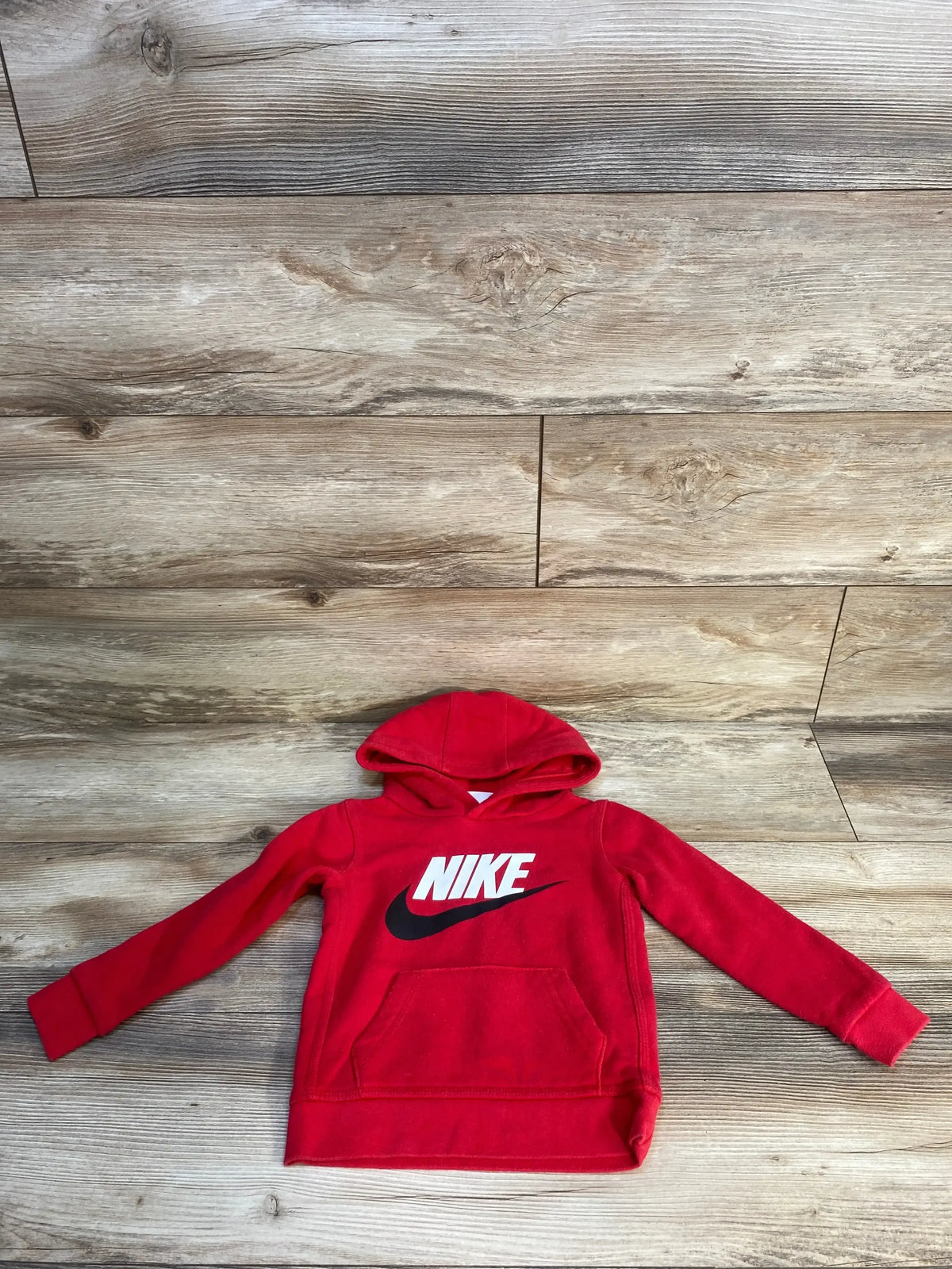 Red Nike kids hoodie with white logo and front pocket on wooden floor background