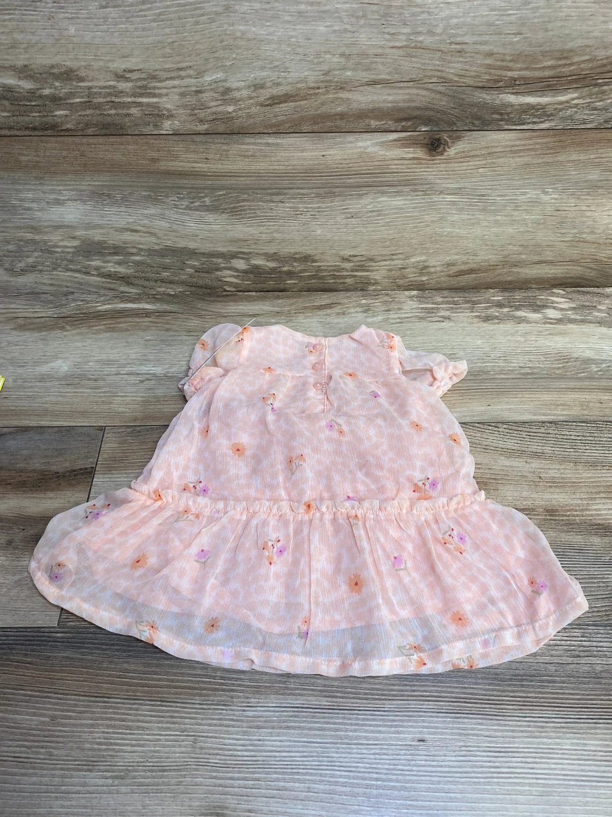 Flat lay of pink floral baby dress showing short flutter sleeves, gathered waist and ruffle hem on light wood background