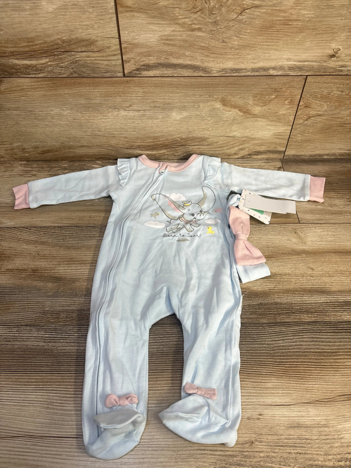 Front view of blue Disney Baby Dumbo sleeper and matching headband showcasing Dumbo graphic with wood floor background
