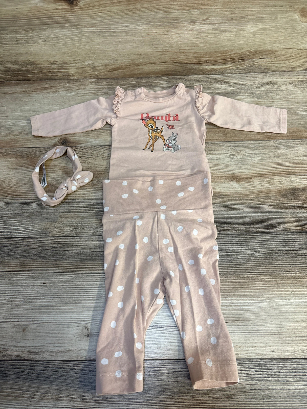 Pink baby outfit set with Bambi graphic, polka dot pants, and matching headband on wood background