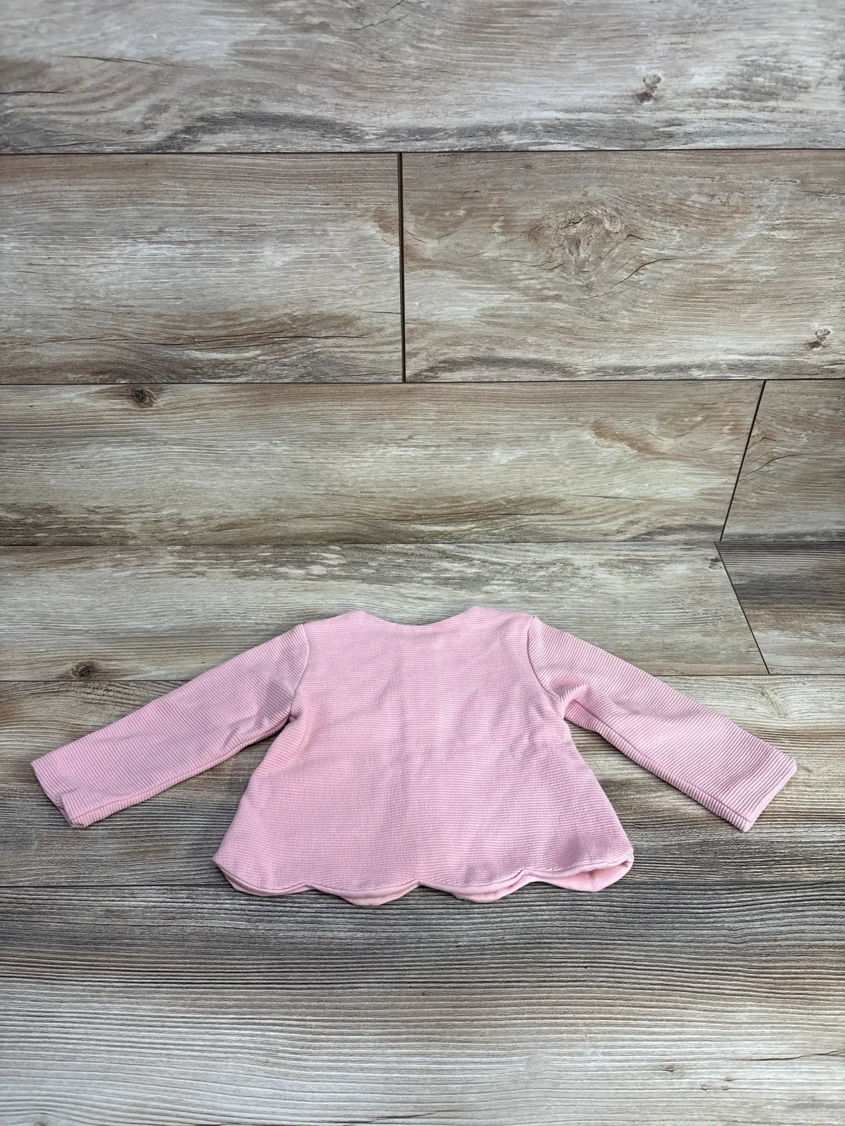 Back view of pink ribbed full-zip baby jacket size 6-9m showcasing scalloped hem with wood floor background