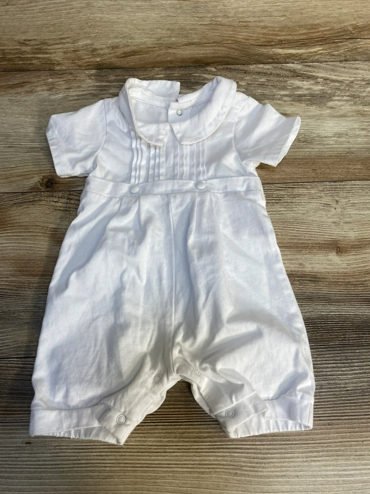 White baby romper with short sleeves, pleated front, and snap buttons on wooden background
