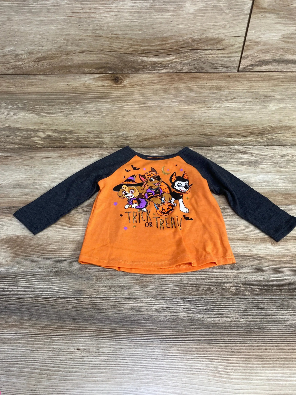 Front view of Paw Patrol raglan toddler shirt with Halloween Trick or Treat graphic and charcoal sleeves on wood background