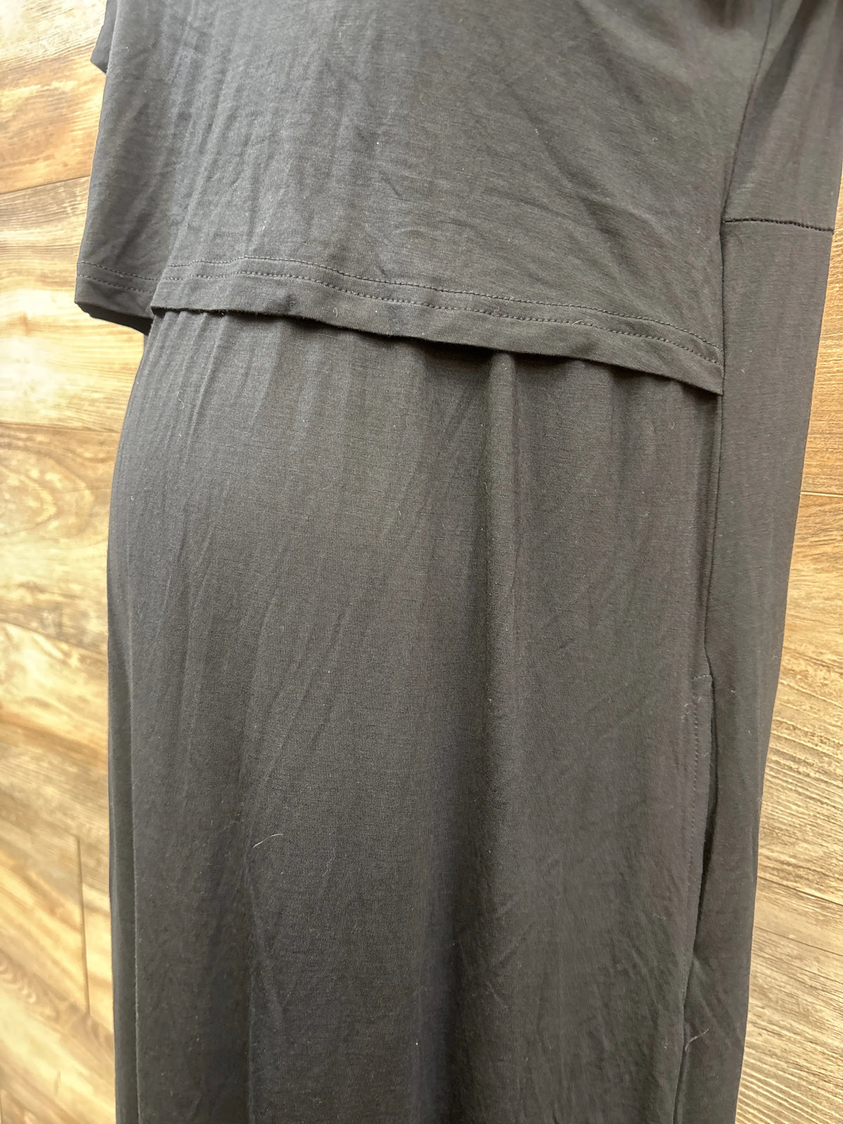 Close-up of black Smallshow maternity nursing dress showcasing layered nursing panel against wood flooring