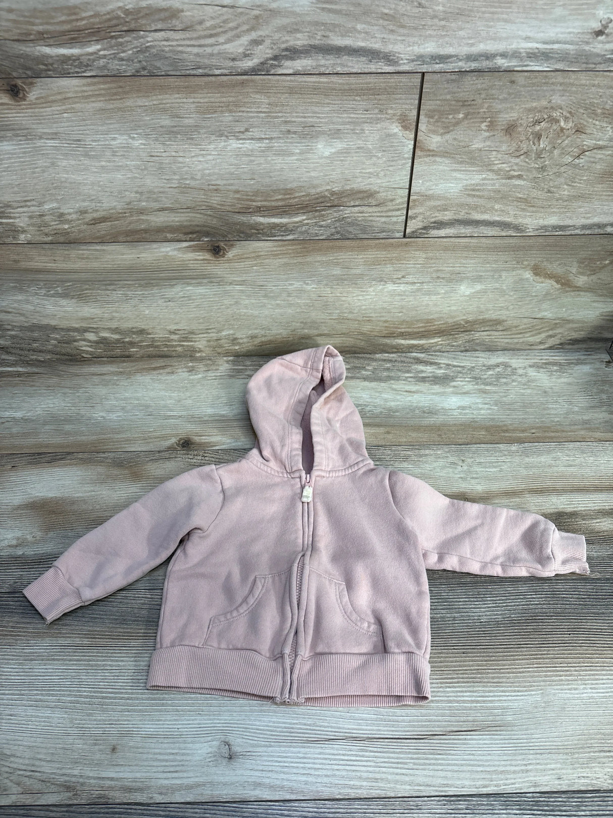 Light pink baby hoodie with zipper and front pockets on wood floor background