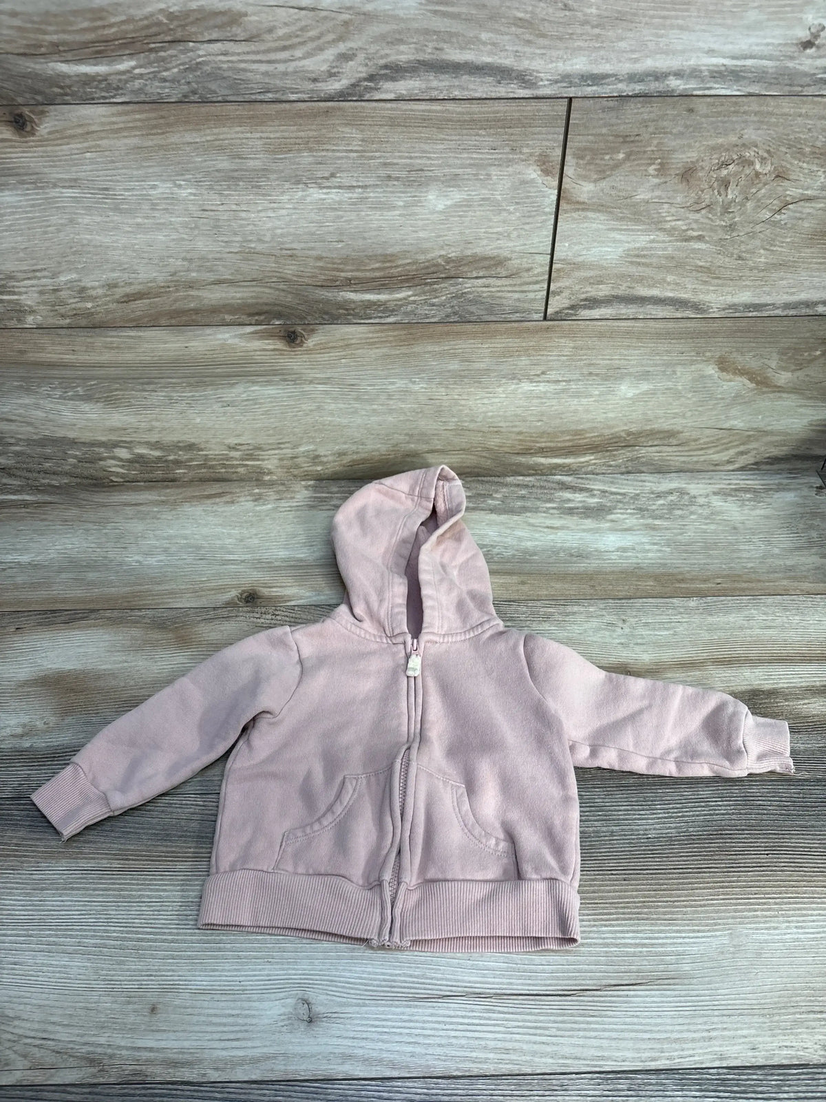 Light pink baby hoodie with zipper and front pockets on wood floor background