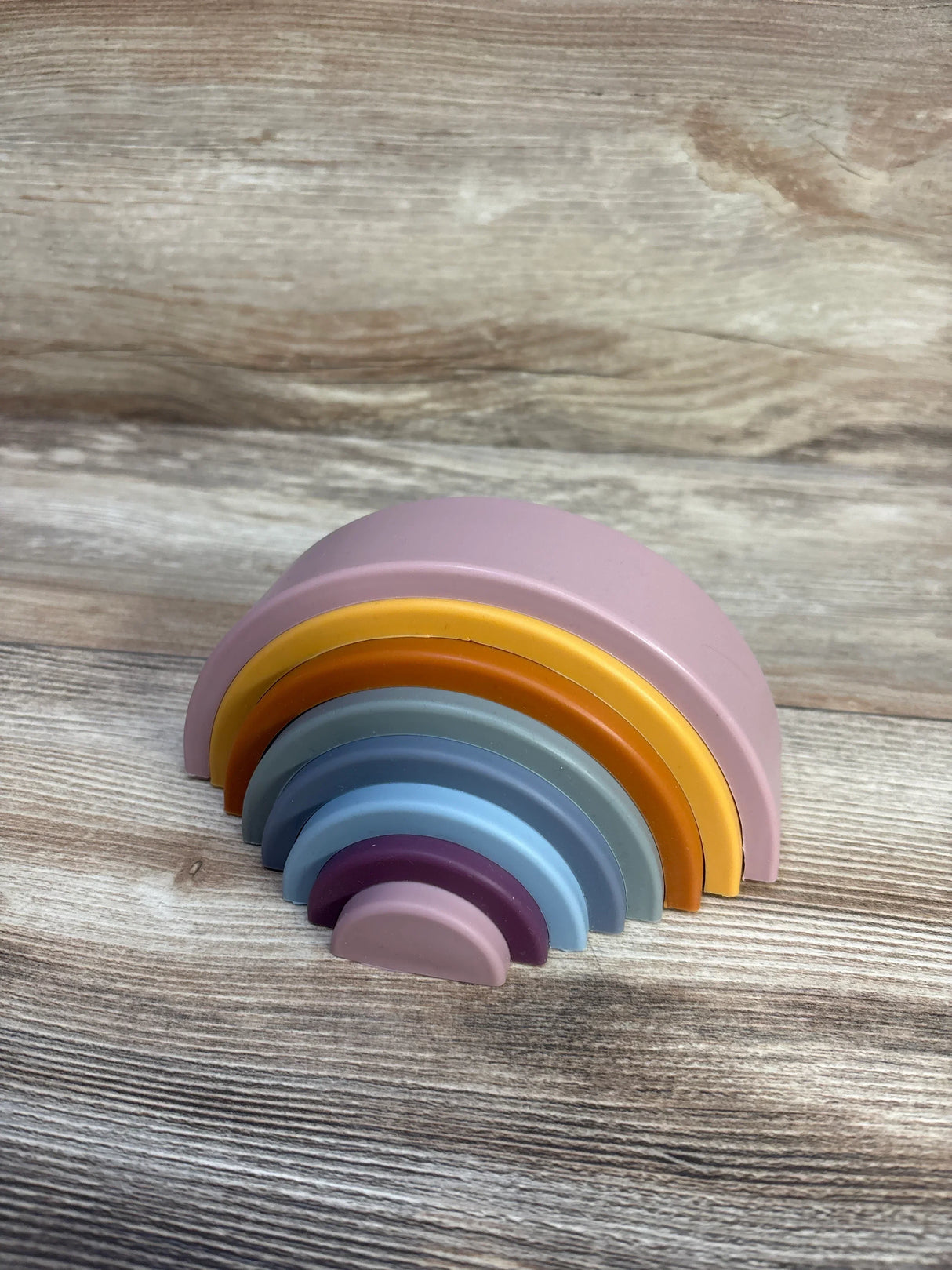Angled view of Twinkle Twinkle Little One silicone rainbow stacker showing stacked pastel silicone arches on wood
