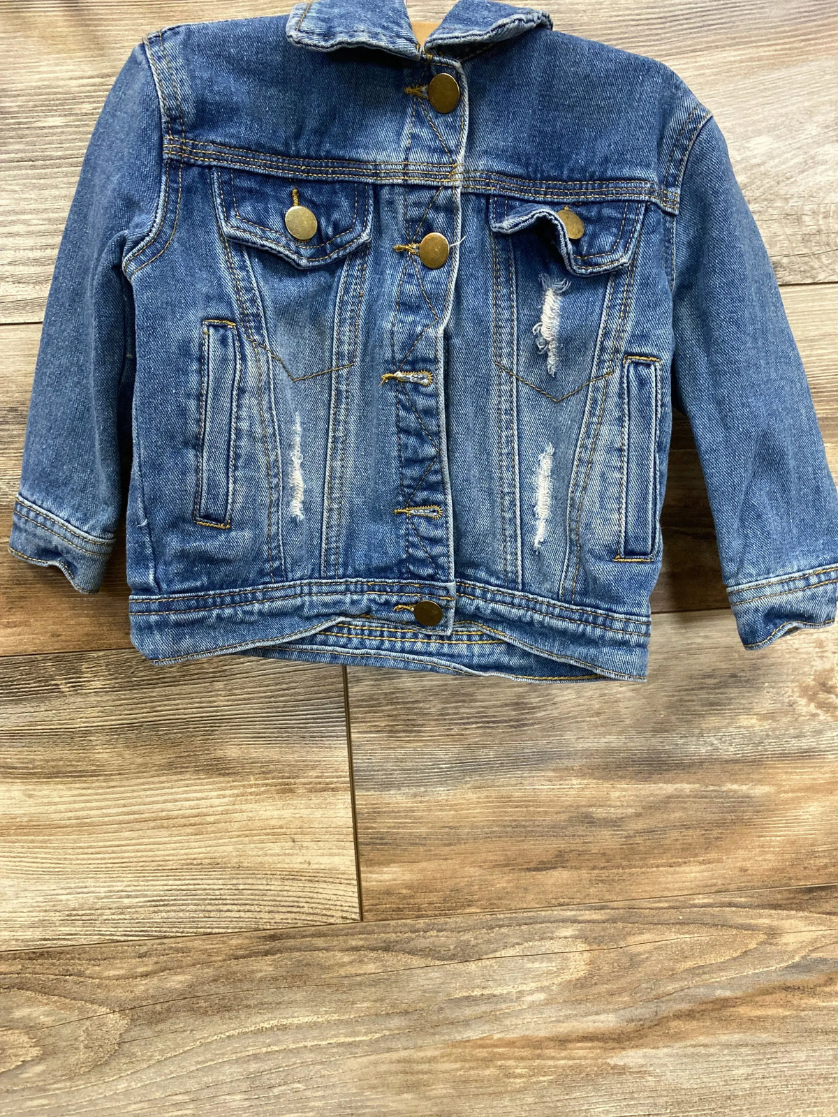 Kids distressed blue denim jacket with brass buttons on wooden background