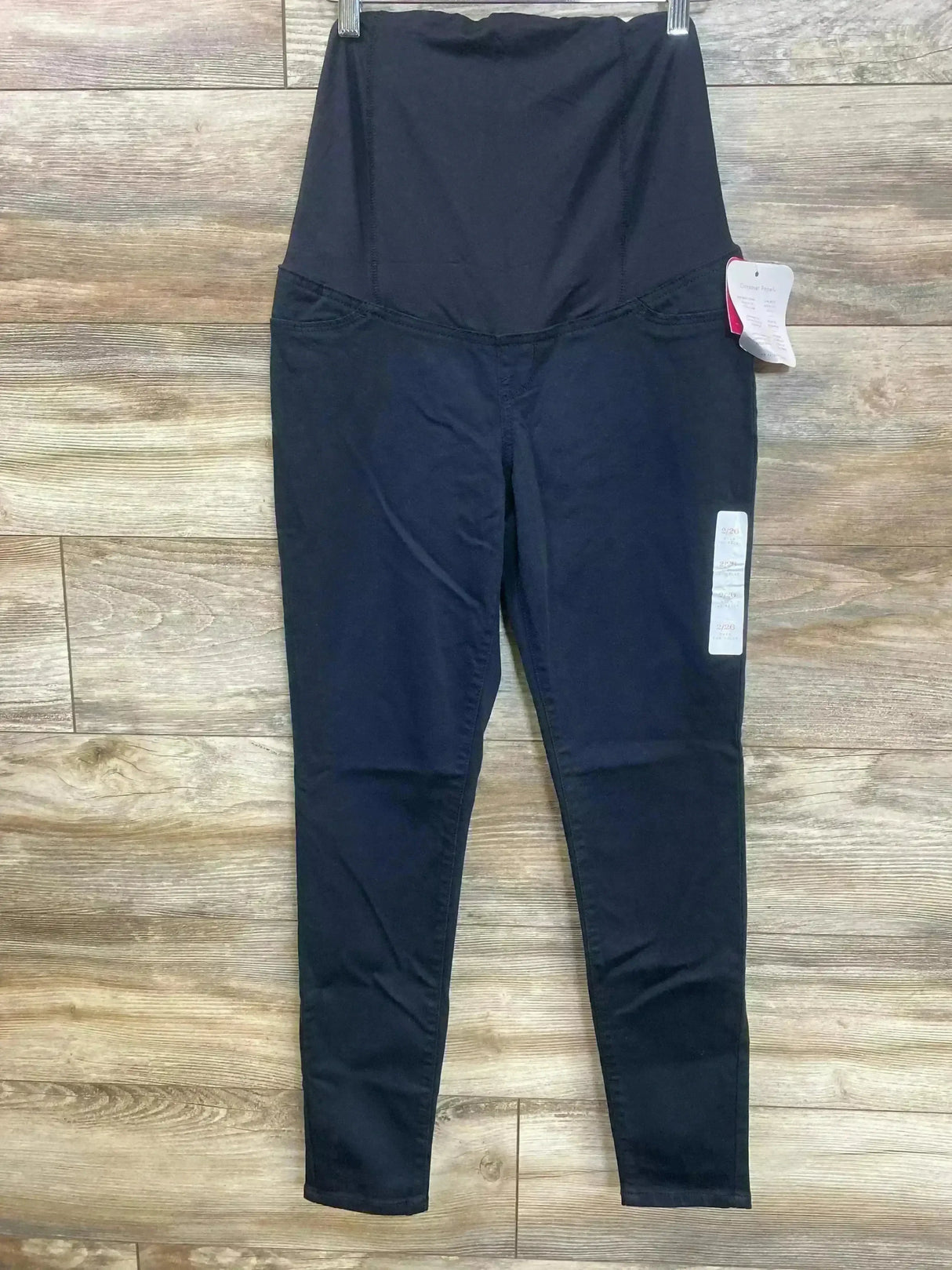 Front view of black Isabel maternity crossover-panel skinny jeans with high-rise belly band on wood floor